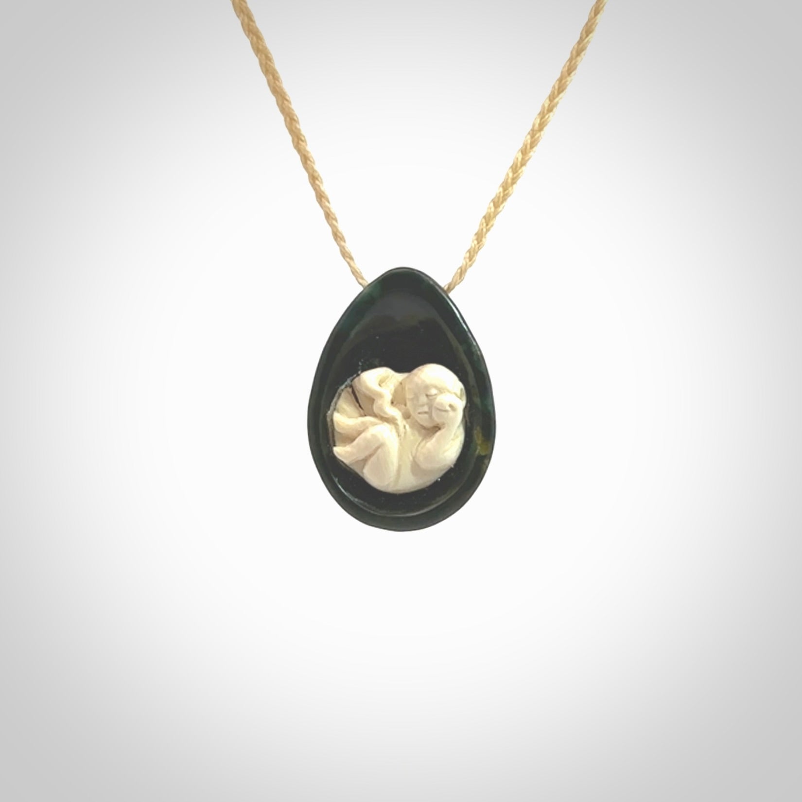 A hand carved baby in the womb pendant made from a jade and bone. This is a work of art carved in jade and bone. We deliver this pendant to you on a plaited cord. Delivery with Express Courier is included in the price.