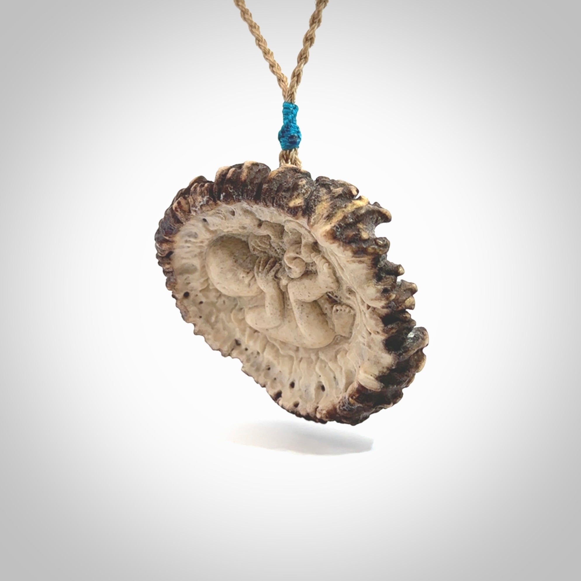 A hand carved baby in the womb pendant made from a piece of deer antler crown. This is a work of art carved in deer antler, bone. We deliver this pendant to you on a plaited tan cord. Delivery with Express Courier is included in the price.