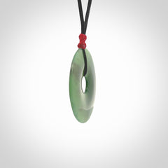 This picture shows a large hand-carved disc pendant. It is carved from British Columbian jade and is suspended from a hand-plaited, black cord. Free delivery worldwide. BC Jade contemporary necklace.