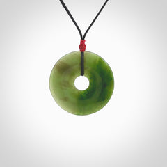 This picture shows a large hand-carved disc pendant. It is carved from British Columbian jade and is suspended from a hand-plaited, black cord. Free delivery worldwide. BC Jade contemporary necklace.