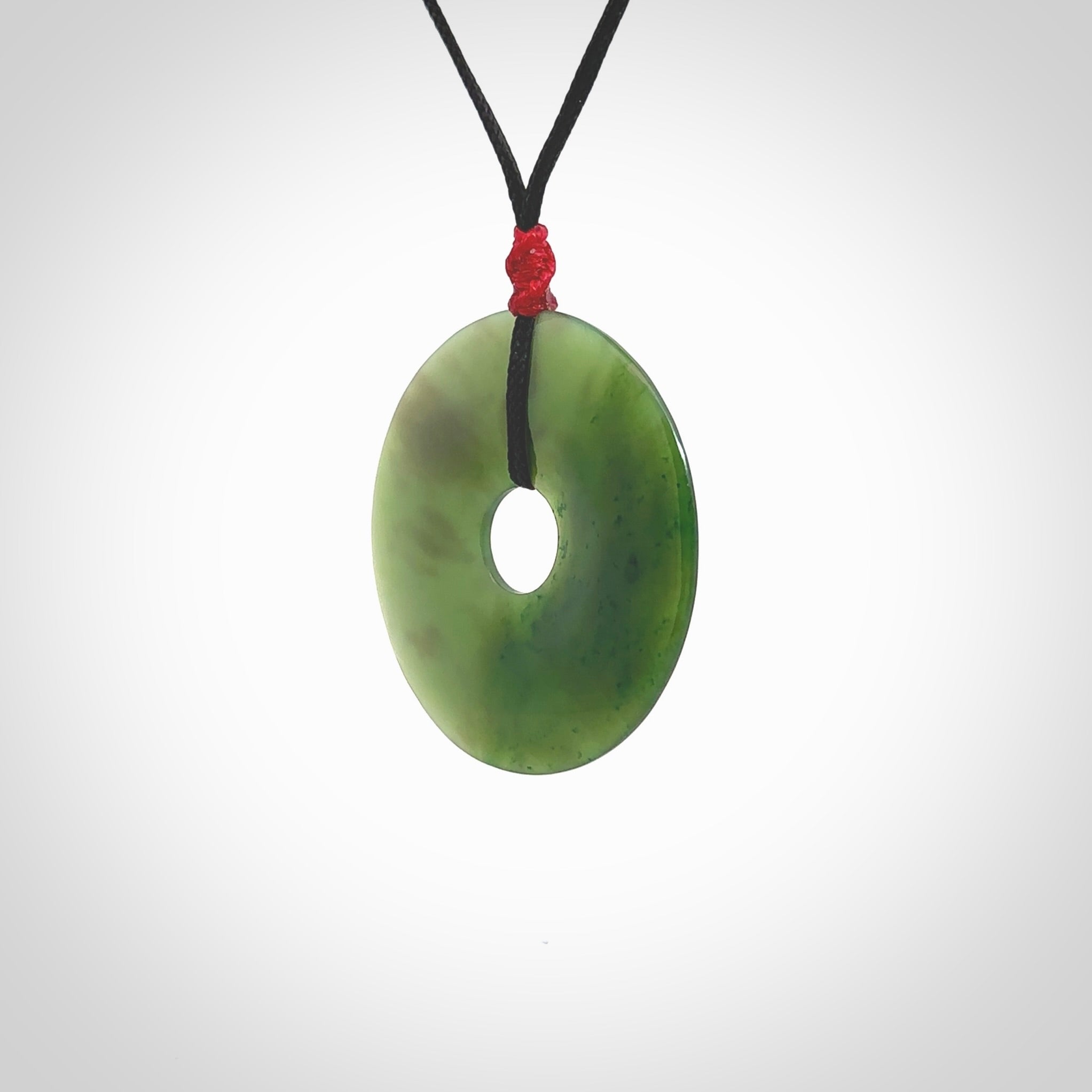 This picture shows a large hand-carved disc pendant. It is carved from British Columbian jade and is suspended from a hand-plaited, black cord. Free delivery worldwide. BC Jade contemporary necklace.