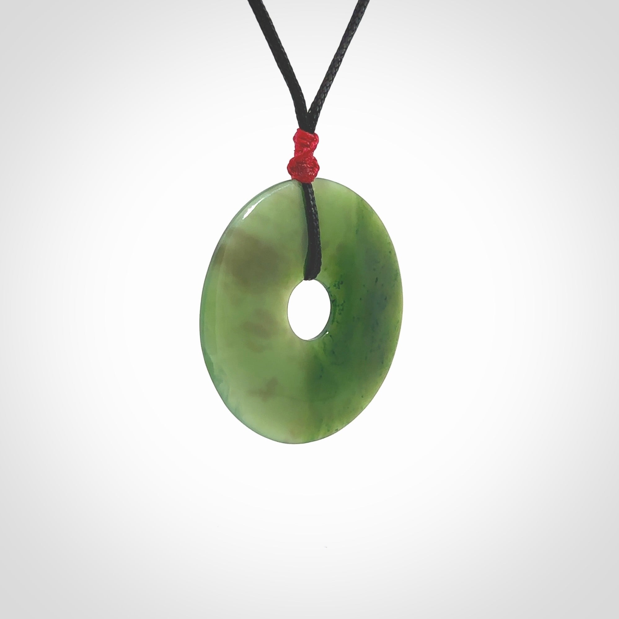 This picture shows a large hand-carved disc pendant. It is carved from British Columbian jade and is suspended from a hand-plaited, black cord. Free delivery worldwide. BC Jade contemporary necklace.