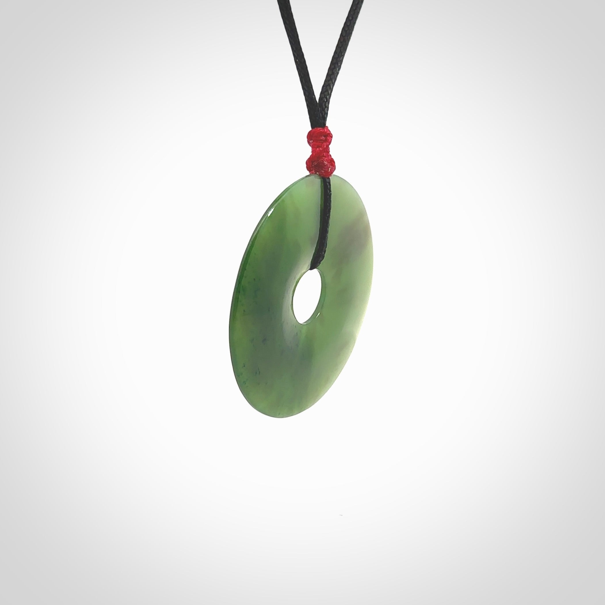 This picture shows a large hand-carved disc pendant. It is carved from British Columbian jade and is suspended from a hand-plaited, black cord. Free delivery worldwide. BC Jade contemporary necklace.