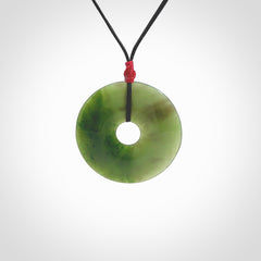 This picture shows a large hand-carved disc pendant. It is carved from British Columbian jade and is suspended from a hand-plaited, black cord. Free delivery worldwide. BC Jade contemporary necklace.