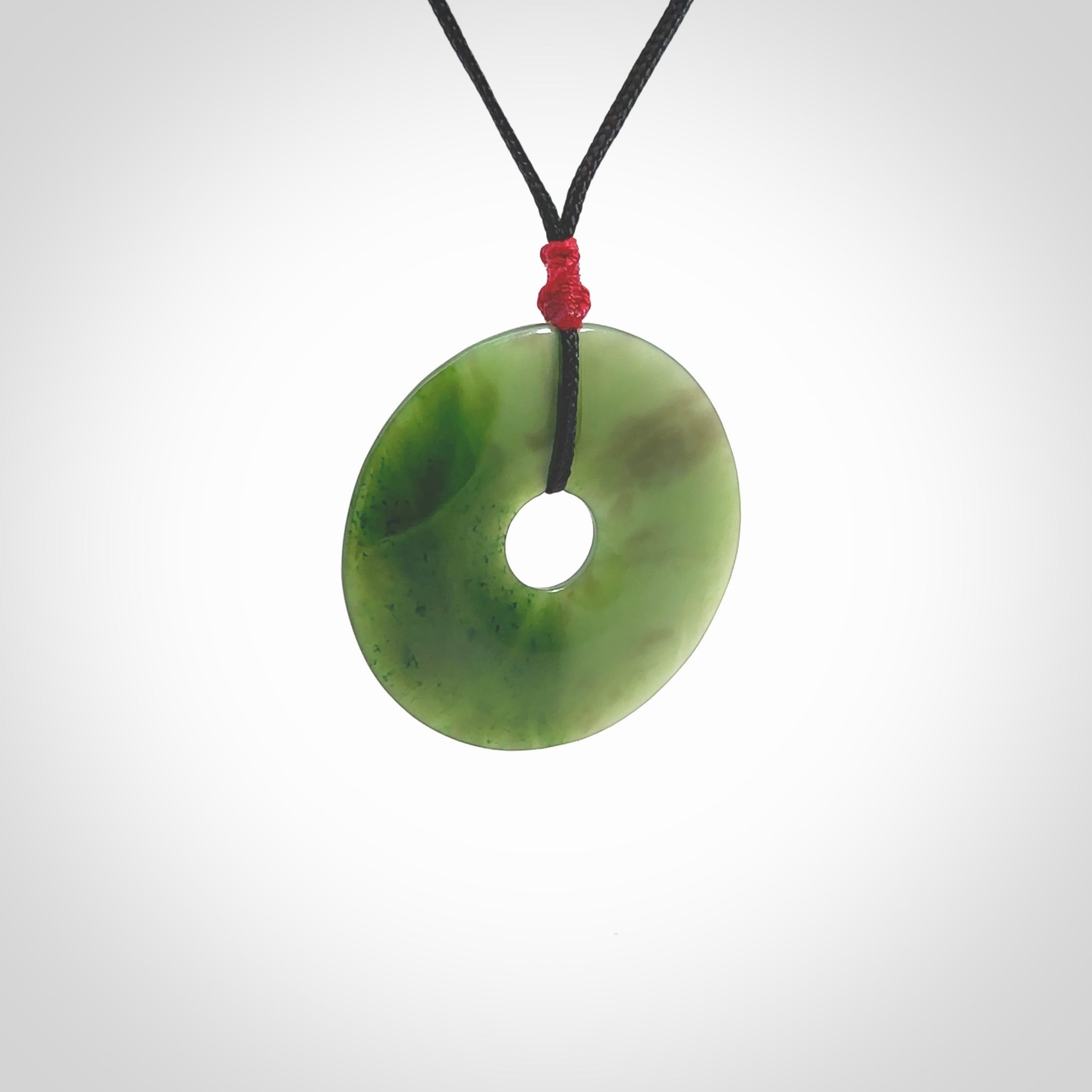 This picture shows a large hand-carved disc pendant. It is carved from British Columbian jade and is suspended from a hand-plaited, black cord. Free delivery worldwide. BC Jade contemporary necklace.