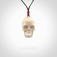 This picture shows a large sized Deer Antler Bone skull pendant that we have hand carved. It is polished to a soft shine and is a very striking piece. The cord is black and has a small red popper binding just above the pendant.