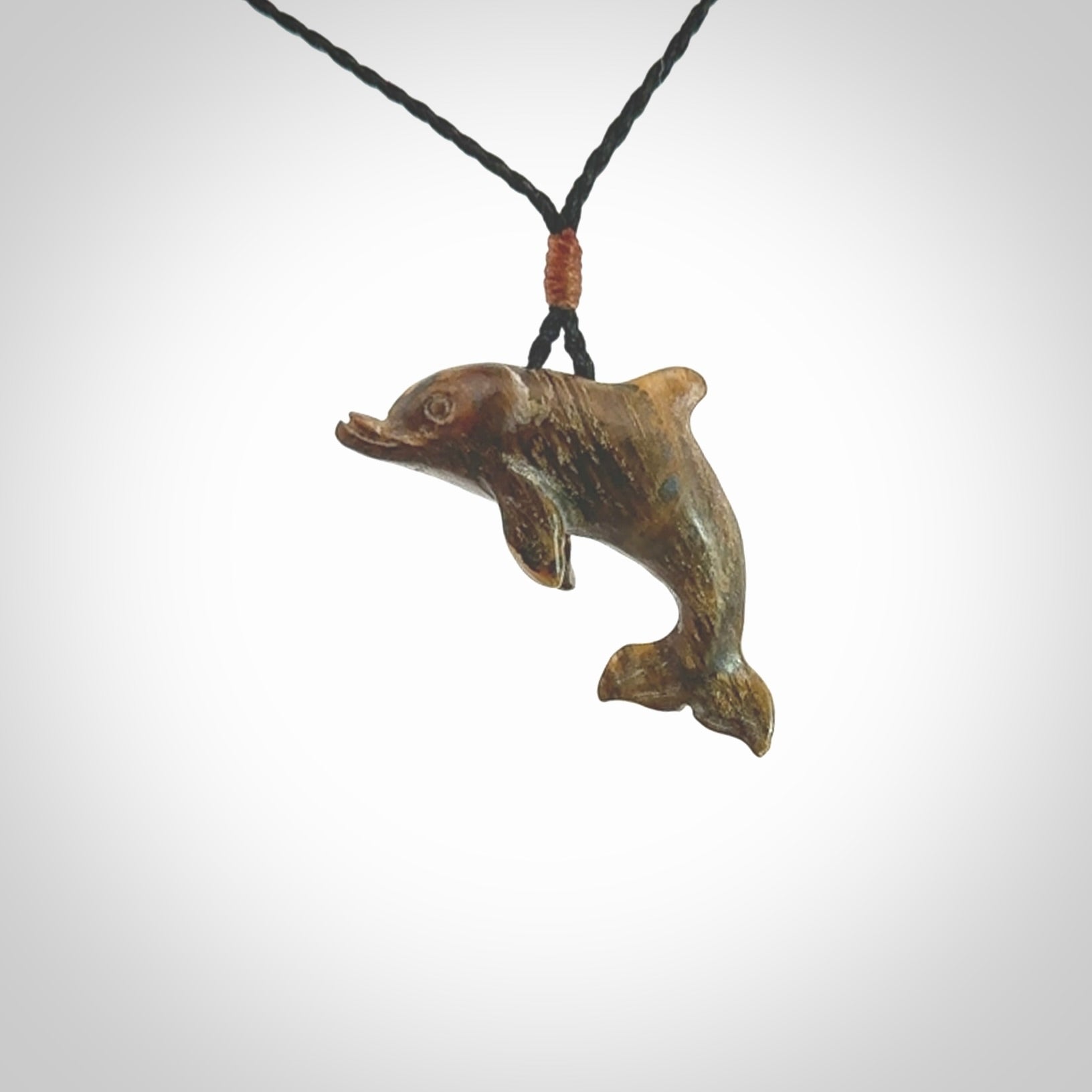 This is a hand carved dolphin pendant made from a gorgeous and striking piece of Tiger Iron. This is a superbly carved and very unique dolphin necklace. For sale online from NZ Pacific. Delivered with adjustable cord.