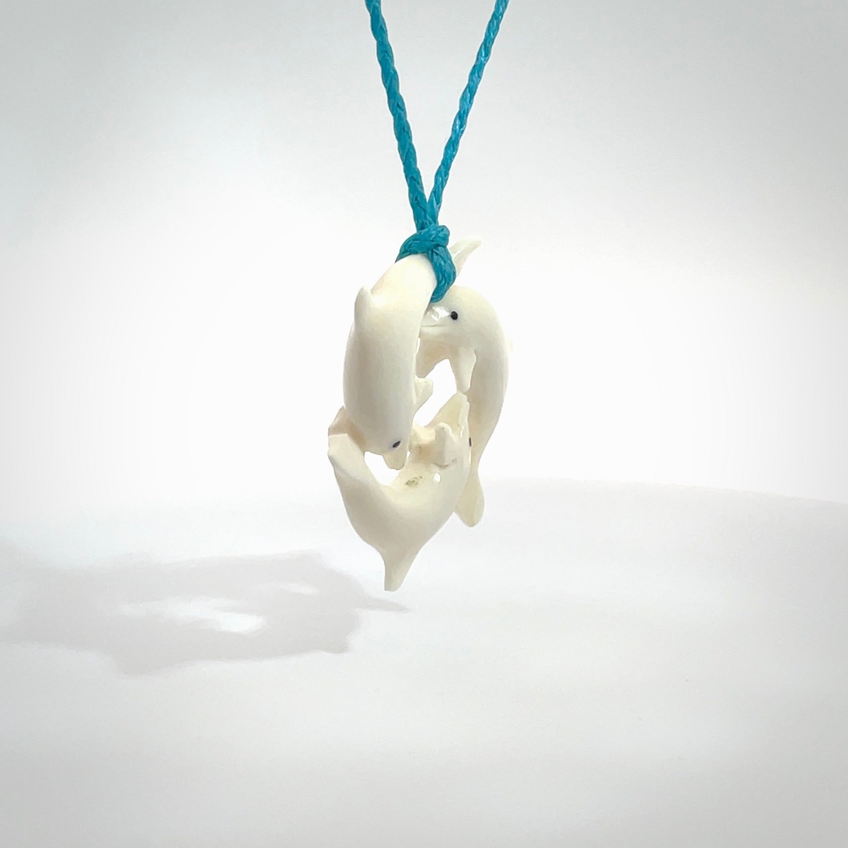 Hand carved dolphin trio pendant, made from natural bone by NZ Pacific. Hand made natural bone dolphin trilogy necklace, provided with an adjustable paradise blue cord. Packaged in a woven kete pouch.