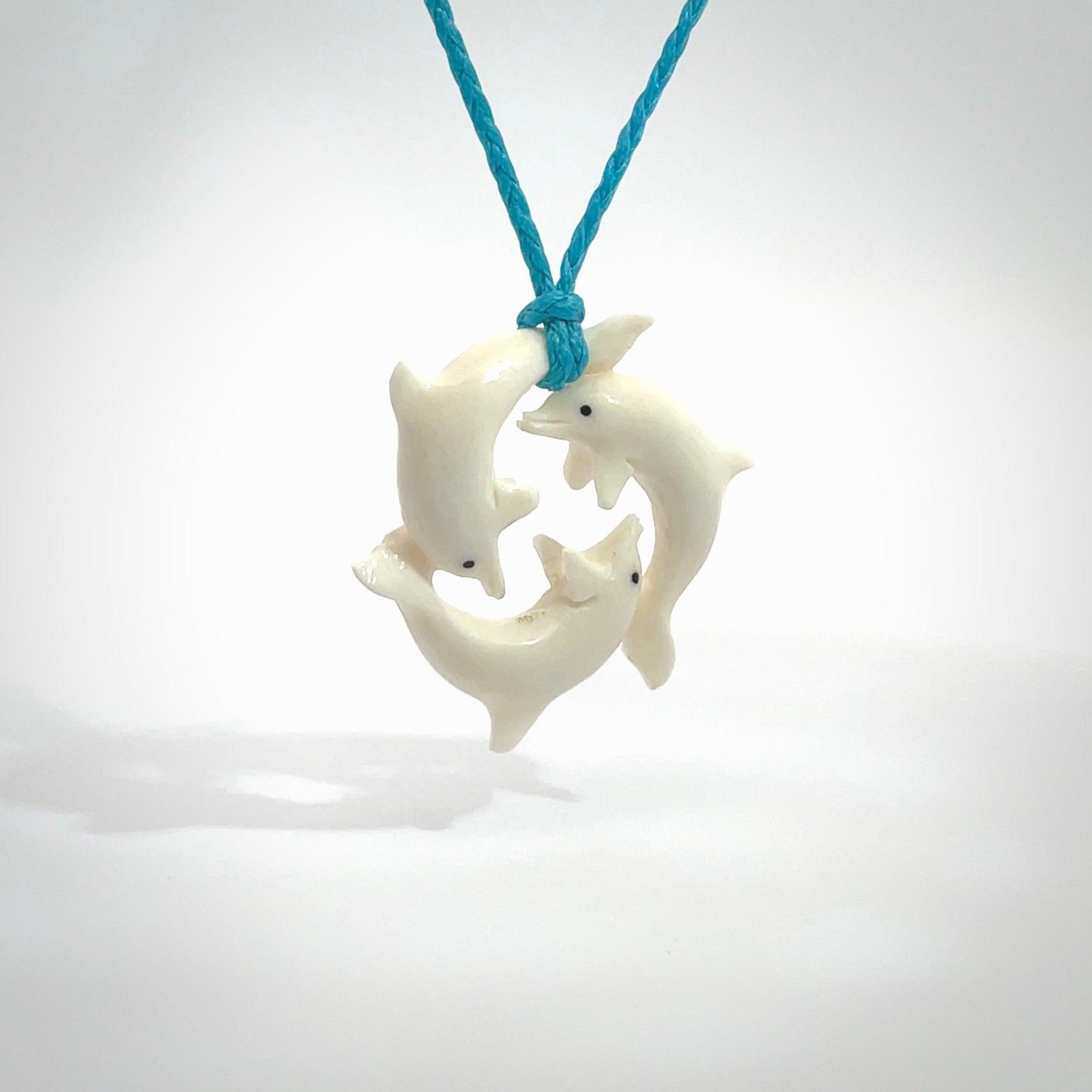 Hand carved dolphin trio pendant, made from natural bone by NZ Pacific. Hand made natural bone dolphin trilogy necklace, provided with an adjustable paradise blue cord. Packaged in a woven kete pouch.