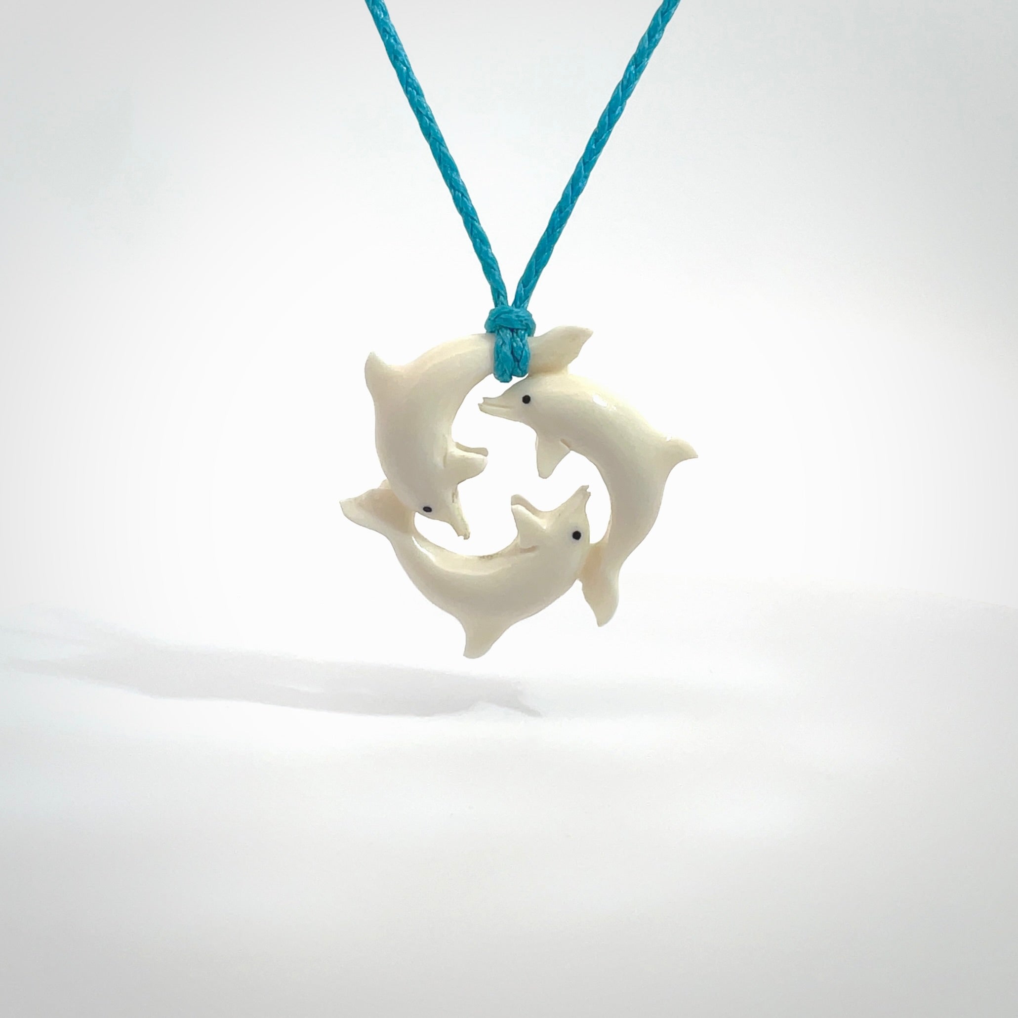 Hand carved dolphin trio pendant, made from natural bone by NZ Pacific. Hand made natural bone dolphin trilogy necklace, provided with an adjustable paradise blue cord. Packaged in a woven kete pouch.