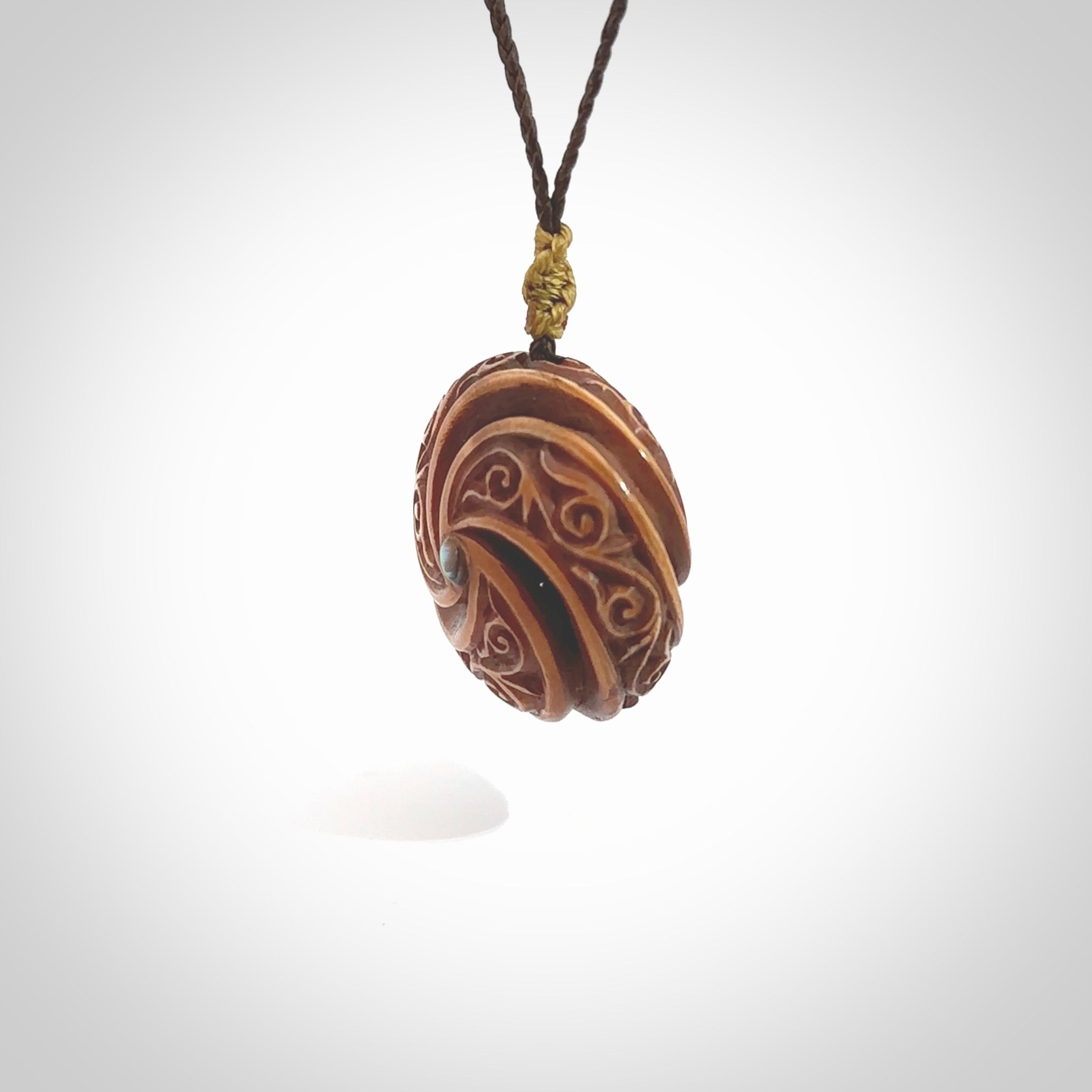 A hand carved and intricate koru pendant made for us by Yuri Terenyi. This is a beautiful little piece and is emblematic of the well known and loved Koru design. It is carved from bone in a hollowed, oval ball shape with decorative design carved into the koru. It is suspended from a chocolate brown cord which is adjustable.