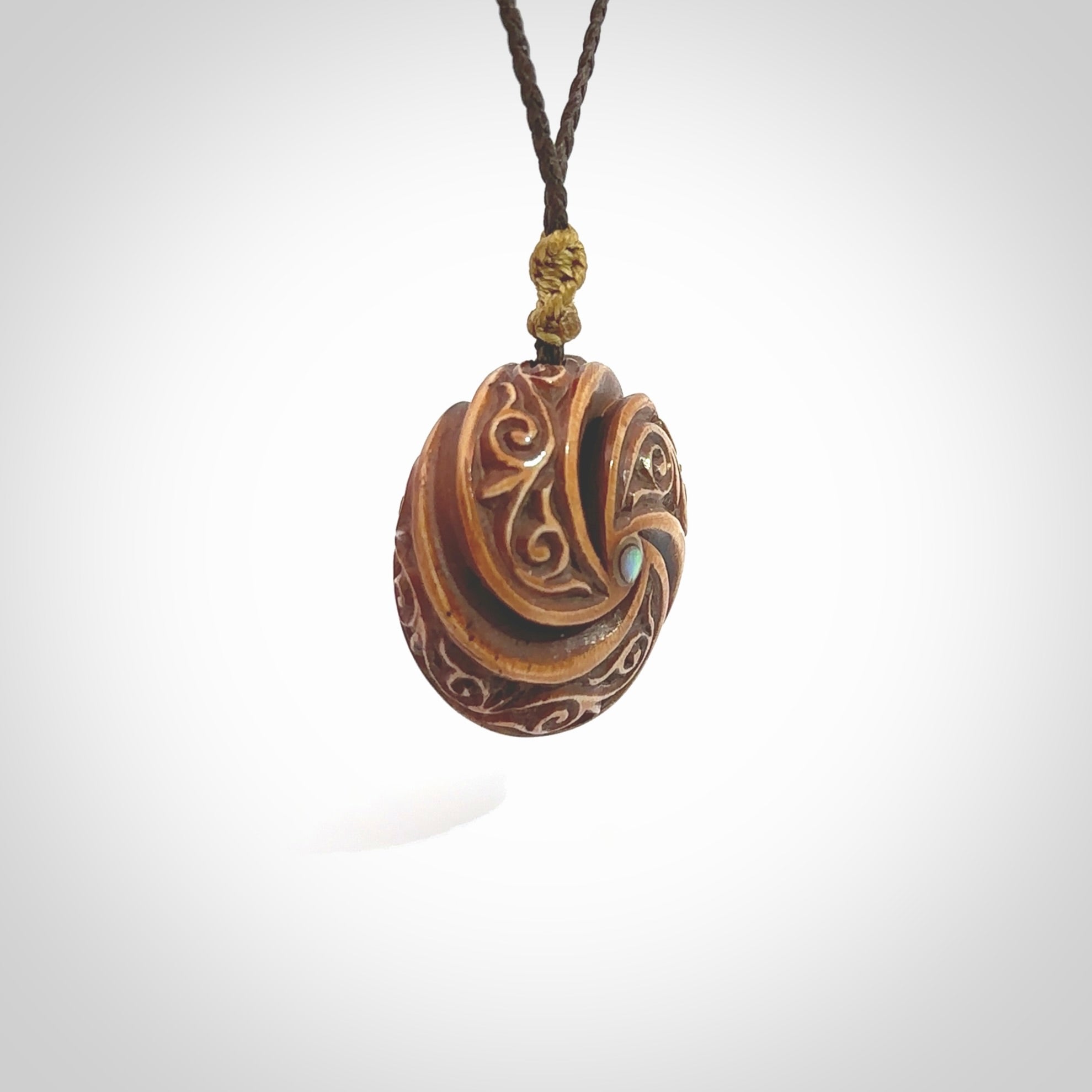 A hand carved and intricate koru pendant made for us by Yuri Terenyi. This is a beautiful little piece and is emblematic of the well known and loved Koru design. It is carved from bone in a hollowed, oval ball shape with decorative design carved into the koru. It is suspended from a chocolate brown cord which is adjustable.