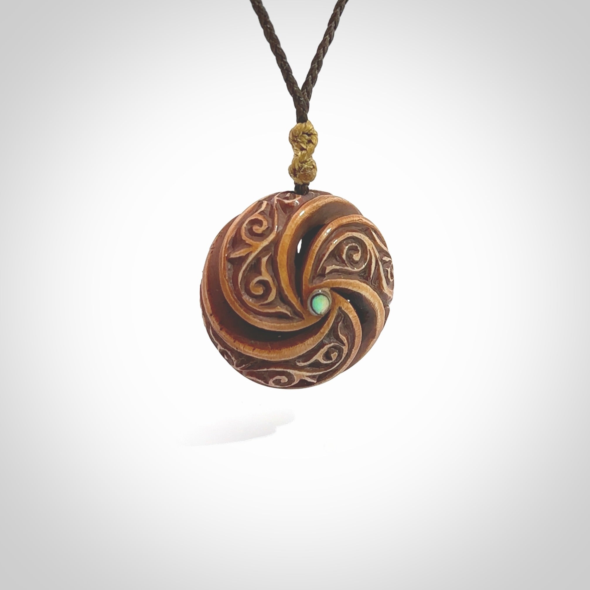 A hand carved and intricate koru pendant made for us by Yuri Terenyi. This is a beautiful little piece and is emblematic of the well known and loved Koru design. It is carved from bone in a hollowed, oval ball shape with decorative design carved into the koru. It is suspended from a chocolate brown cord which is adjustable.