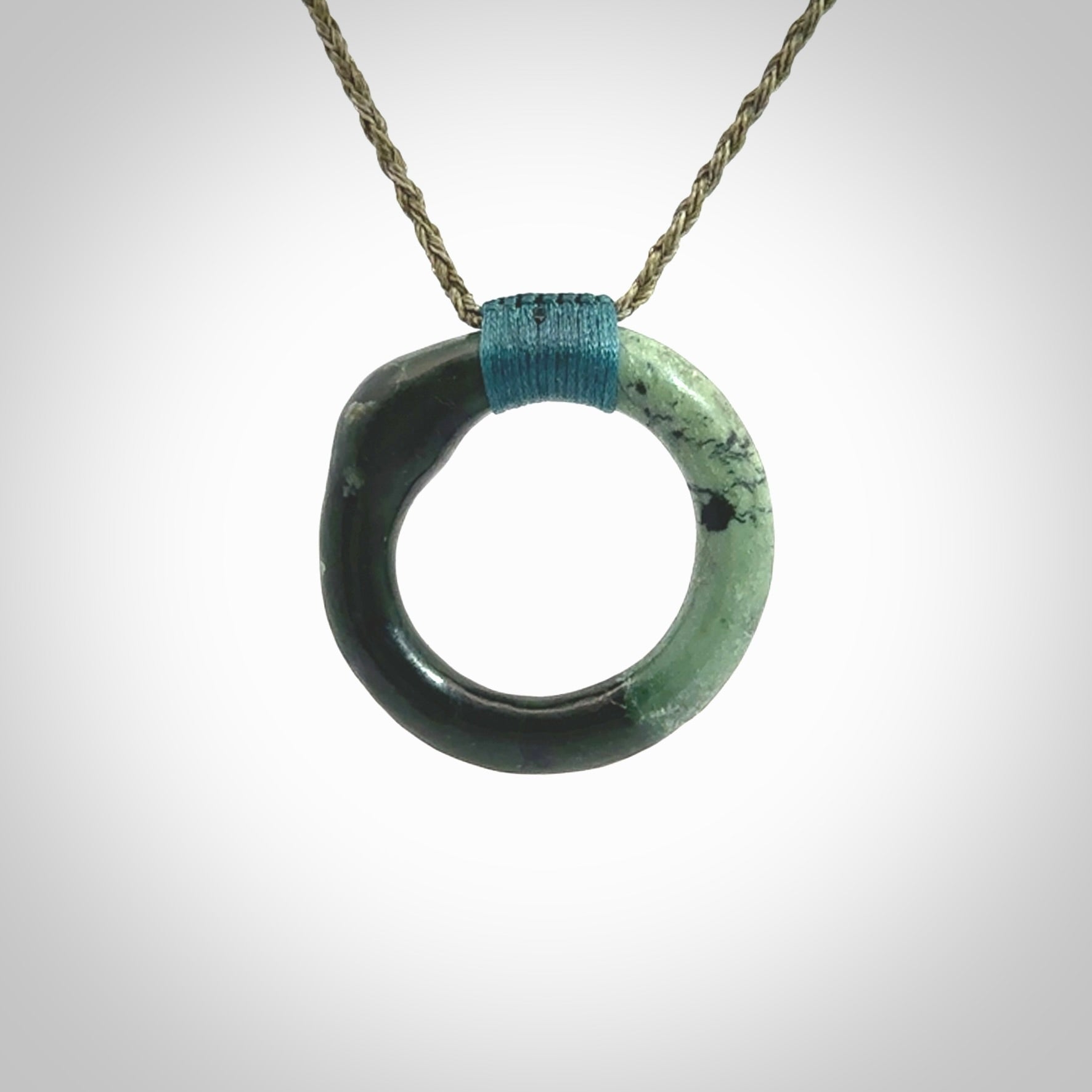 This picture shows a hand carved jade circle pendant with sterling silver inlay. It is suspended from an adjustable khaki coloured cord. Delivery is free worldwide.