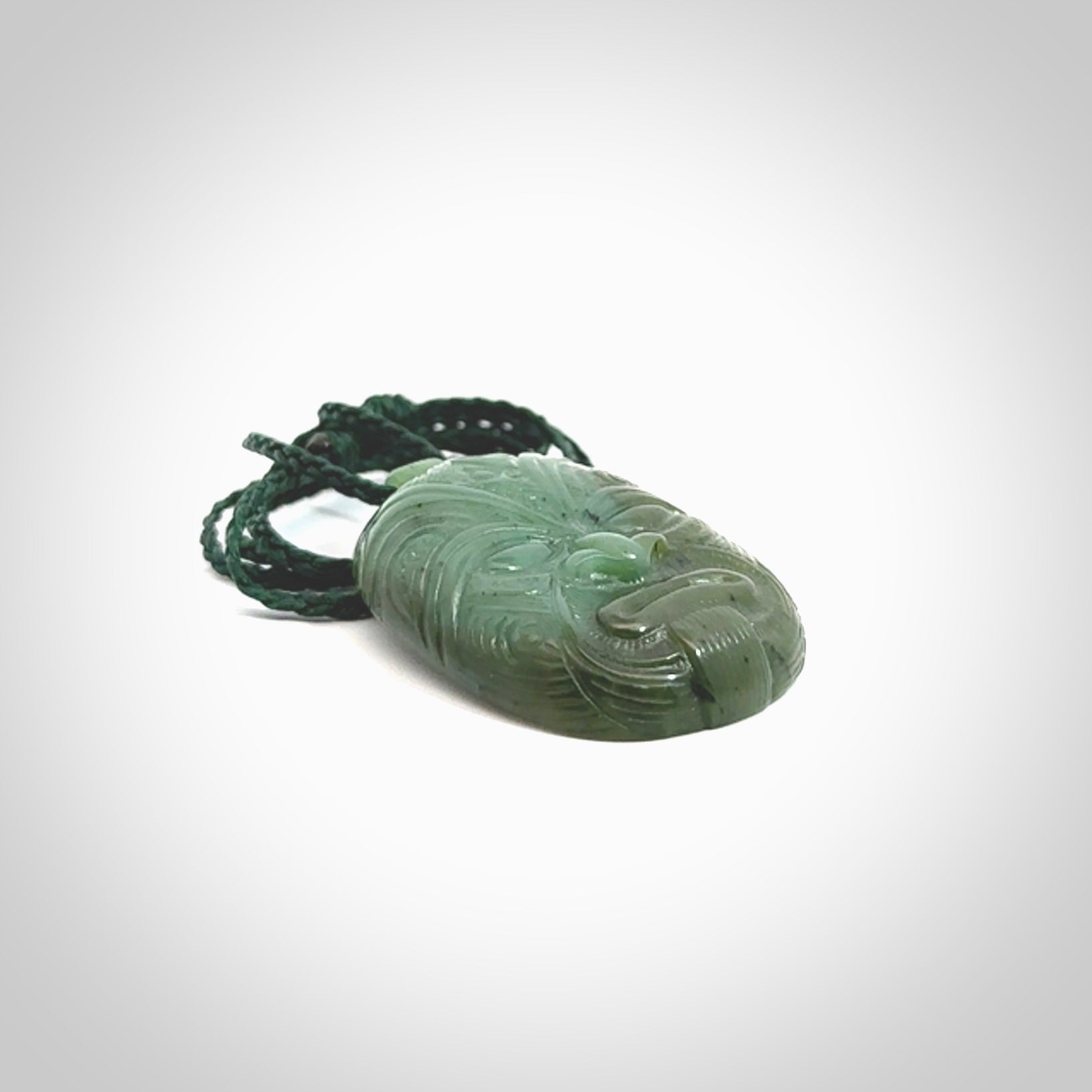 This picture shows a hand carved Jade face pendant. It is a varied green colour which is quite beautiful. Although a medium piece, it is a wonderful, delicate piece of jewellery. The cord is hand plaited and adjustable so that you can position the pendant where it suits you best. Delivery is free worldwide.