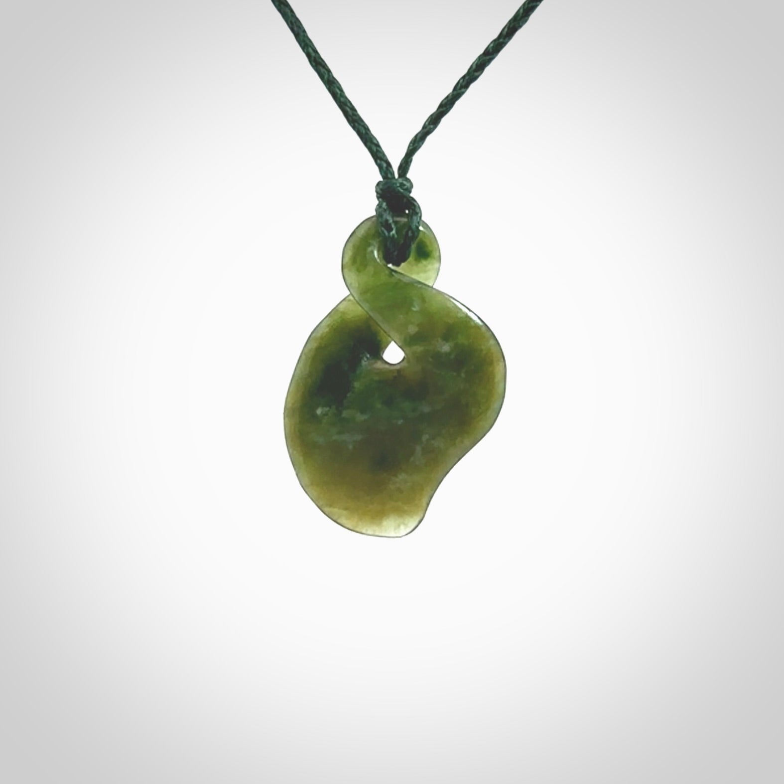 This piece is a fine, delicate drop shaped, single twist pendant. It was carved for us from a lovely semi-translucent green piece of New Zealand jade. It is suspended on an green braided cord that is length adjustable.