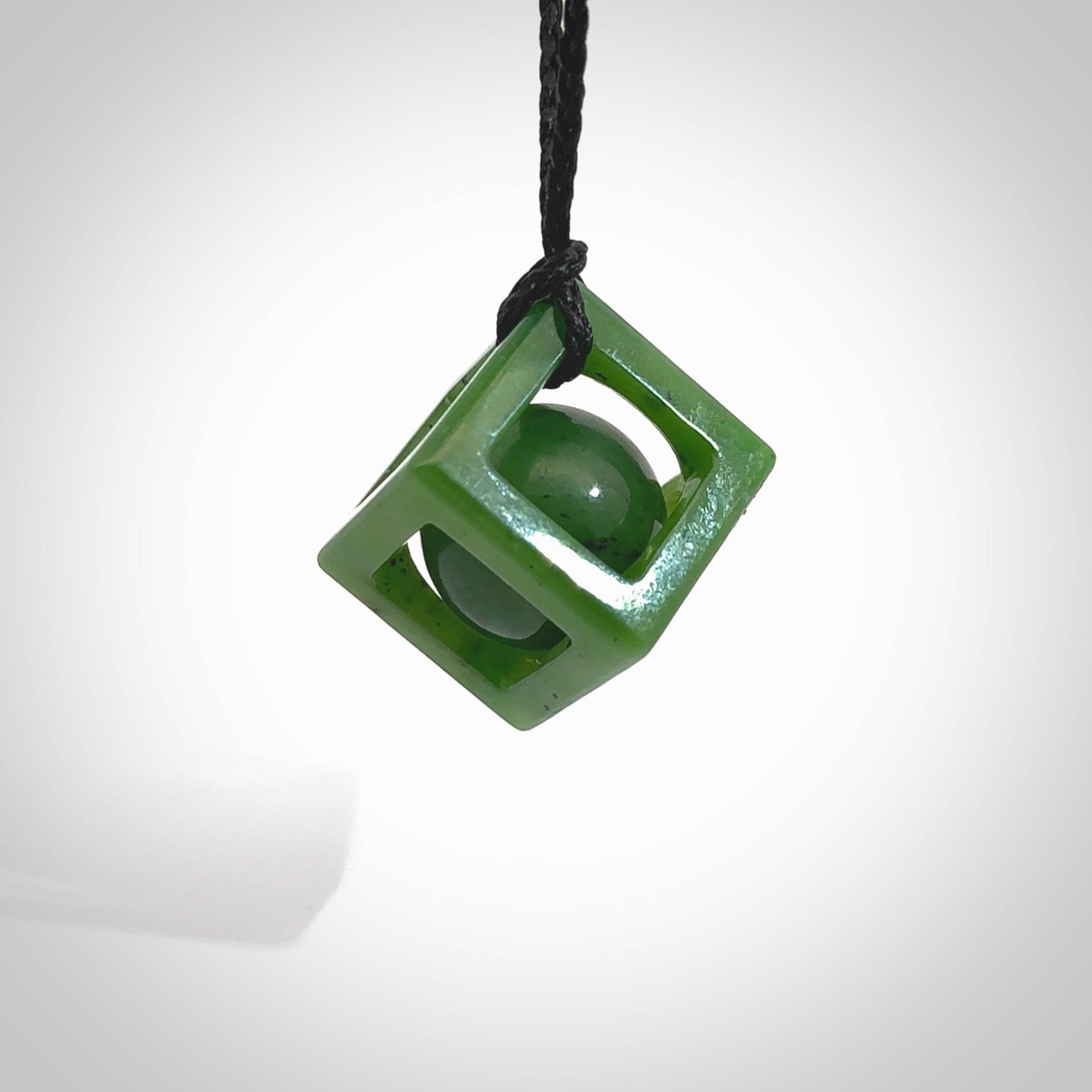 A hand carved medium sized green Jade square box with ball inside necklace. The cord is black and adjustable in length. A medium sized hand made cube/box with ball necklace in green Jade. One off work of art to wear.