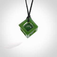 A hand carved medium sized green Jade square box with ball inside necklace. The cord is black and adjustable in length. A medium sized hand made cube/box with ball necklace in green Jade. One off work of art to wear.