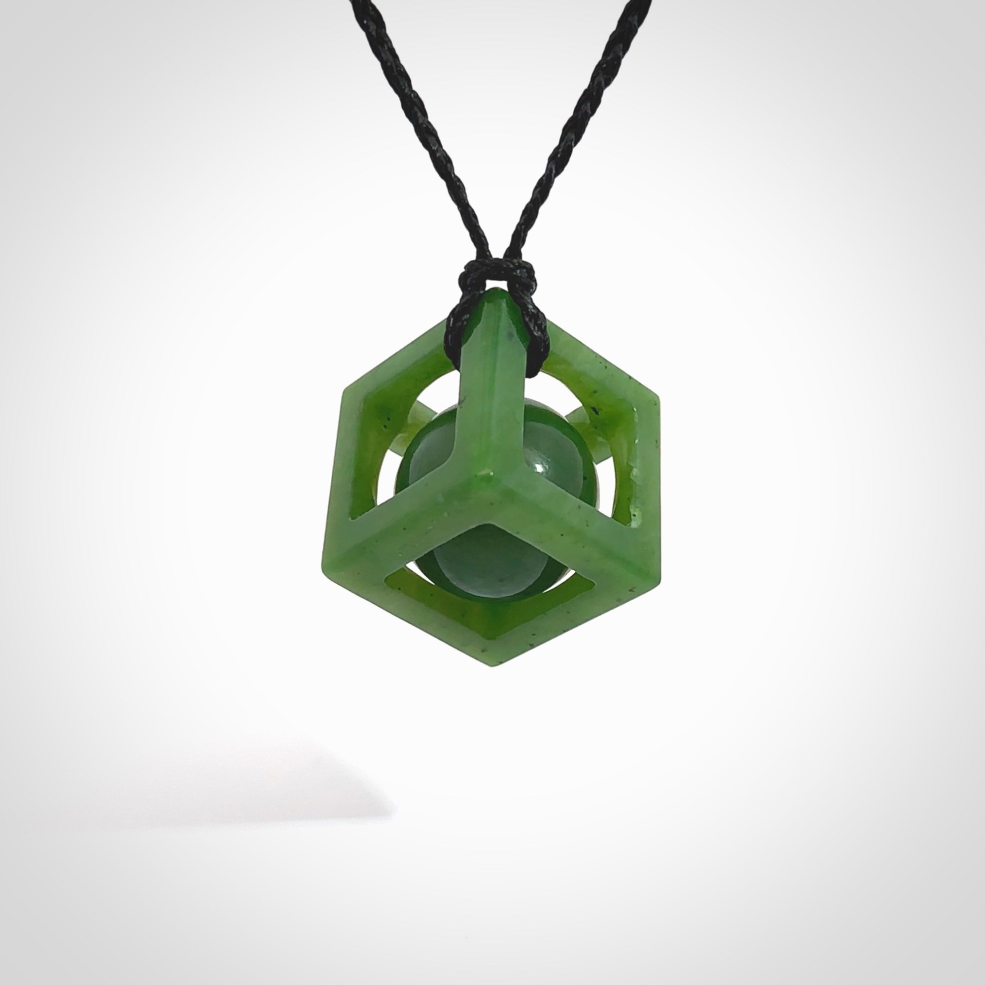 A hand carved medium sized green Jade square box with ball inside necklace. The cord is black and adjustable in length. A medium sized hand made cube/box with ball necklace in green Jade. One off work of art to wear.