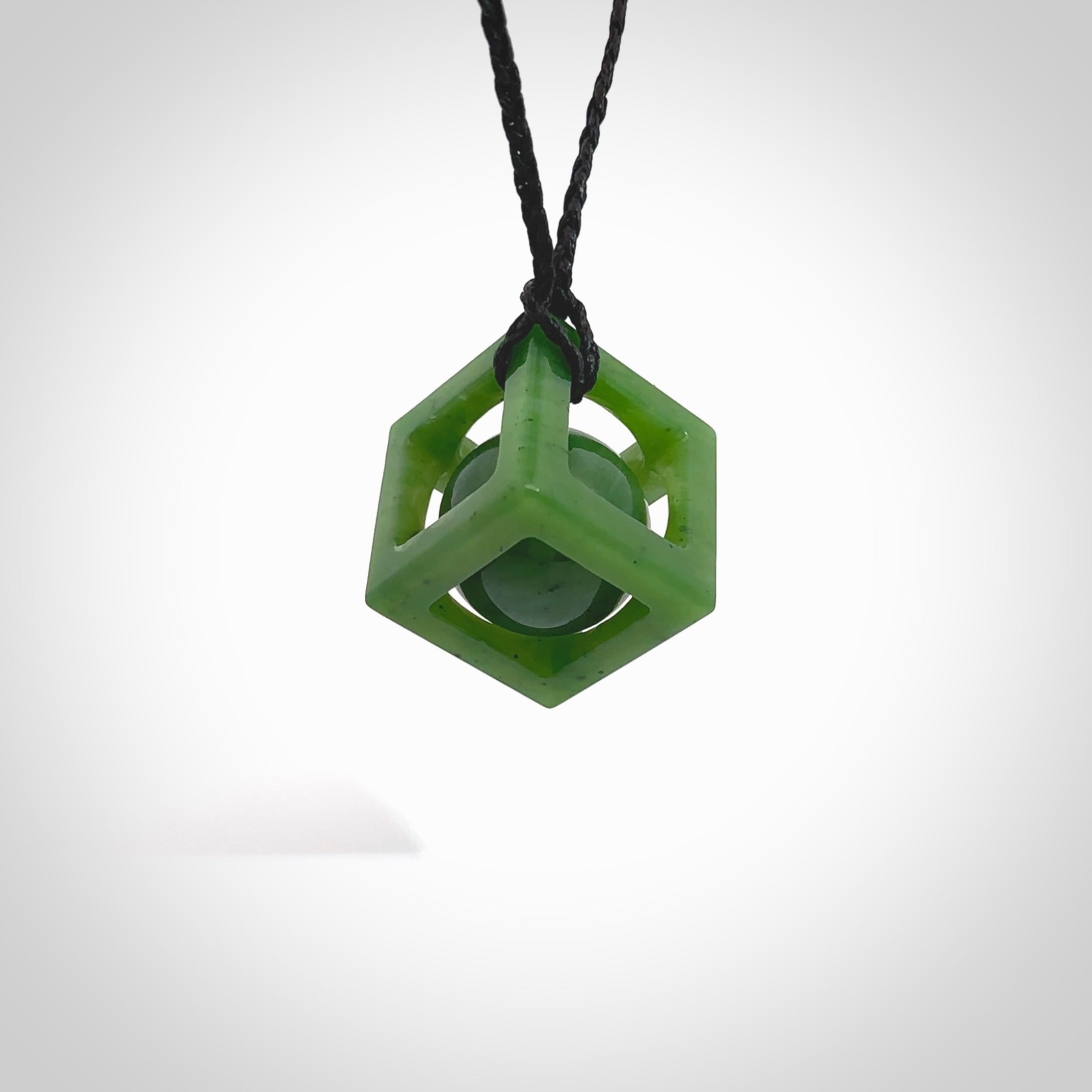 A hand carved medium sized green Jade square box with ball inside necklace. The cord is black and adjustable in length. A medium sized hand made cube/box with ball necklace in green Jade. One off work of art to wear.