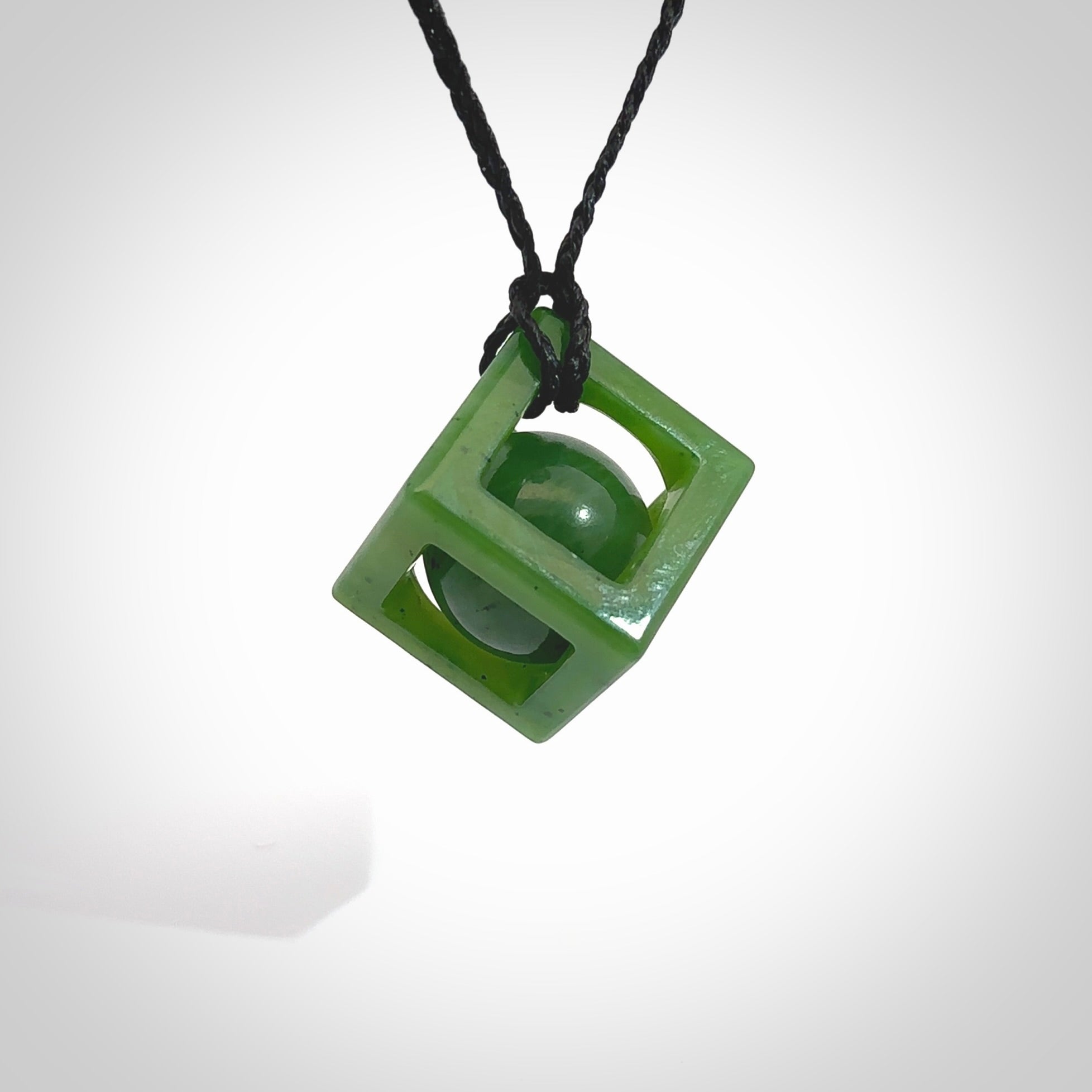 A hand carved medium sized green Jade square box with ball inside necklace. The cord is black and adjustable in length. A medium sized hand made cube/box with ball necklace in green Jade. One off work of art to wear.