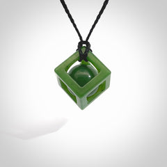 A hand carved medium sized green Jade square box with ball inside necklace. The cord is black and adjustable in length. A medium sized hand made cube/box with ball necklace in green Jade. One off work of art to wear.