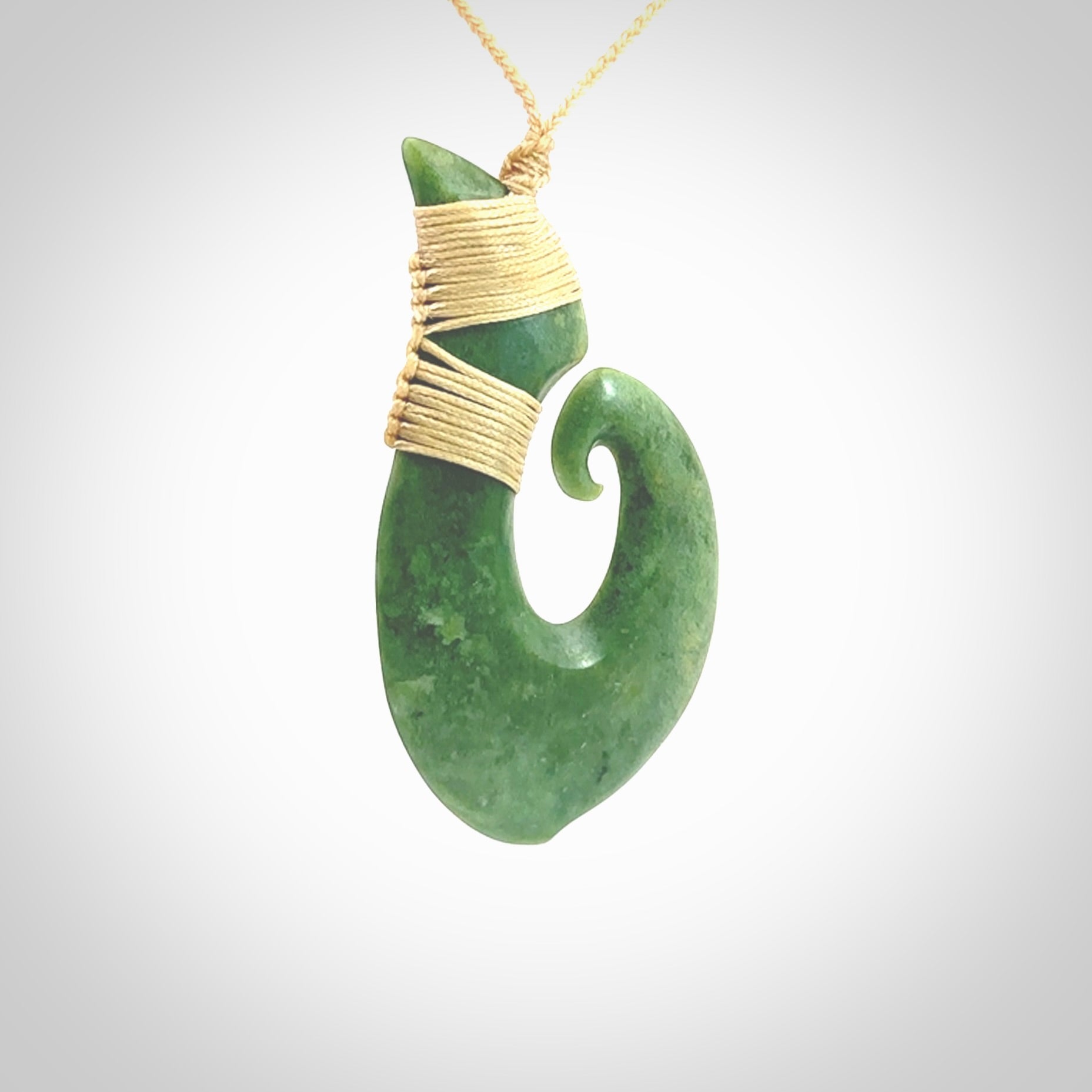 This picture shows a hand carved jade koru pendant. It is a deep green colour and is a wonderful, large sized piece of jewellery. The cord is a four plait beige colour and adjustable so that you can position the pendant where it suits you best. This koru was carved for us by Ric Moor. Delivery is free worldwide.