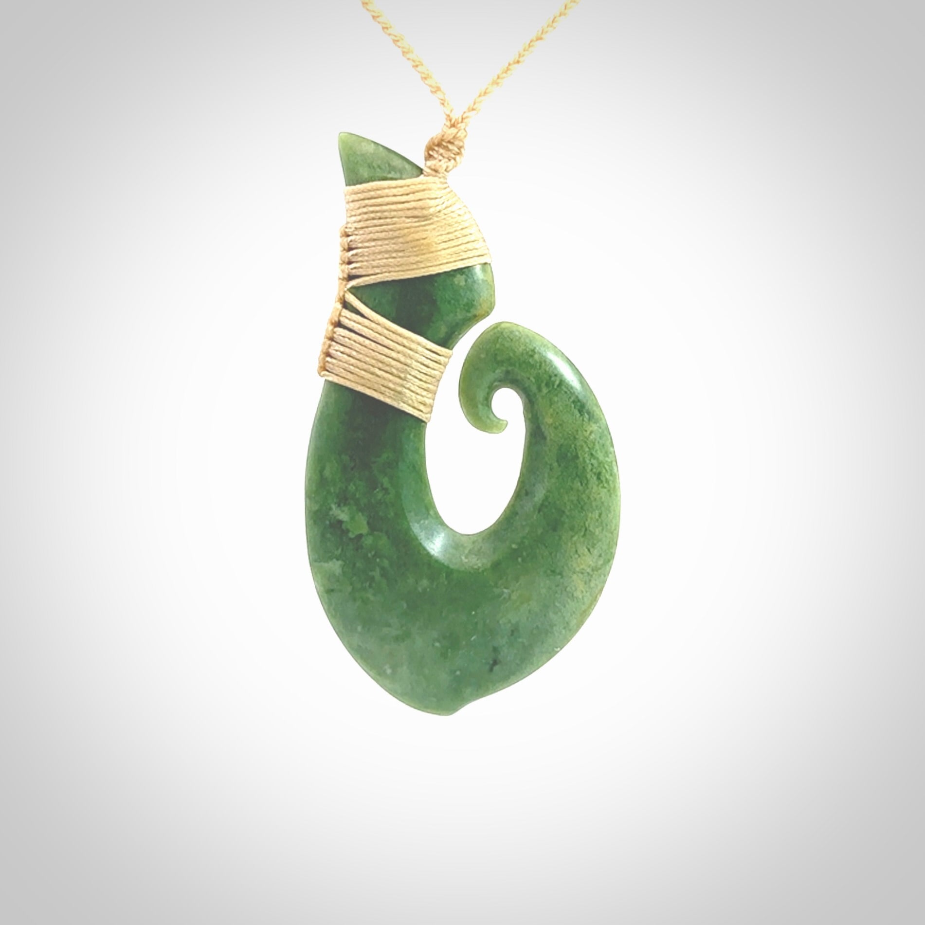 This picture shows a hand carved jade koru pendant. It is a deep green colour and is a wonderful, large sized piece of jewellery. The cord is a four plait beige colour and adjustable so that you can position the pendant where it suits you best. This koru was carved for us by Ric Moor. Delivery is free worldwide.