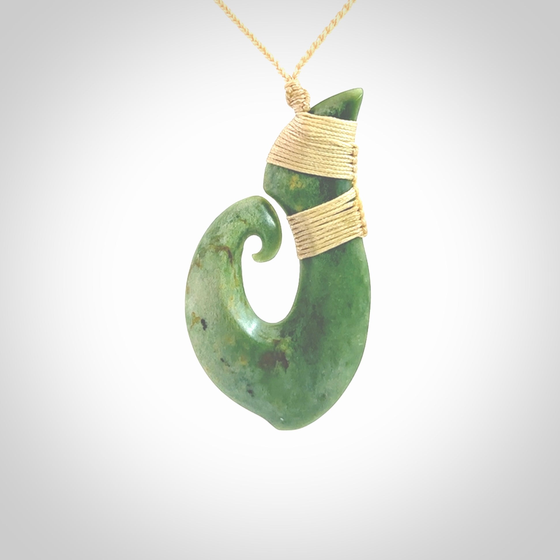 This picture shows a hand carved jade koru pendant. It is a deep green colour and is a wonderful, large sized piece of jewellery. The cord is a four plait beige colour and adjustable so that you can position the pendant where it suits you best. This koru was carved for us by Ric Moor. Delivery is free worldwide.