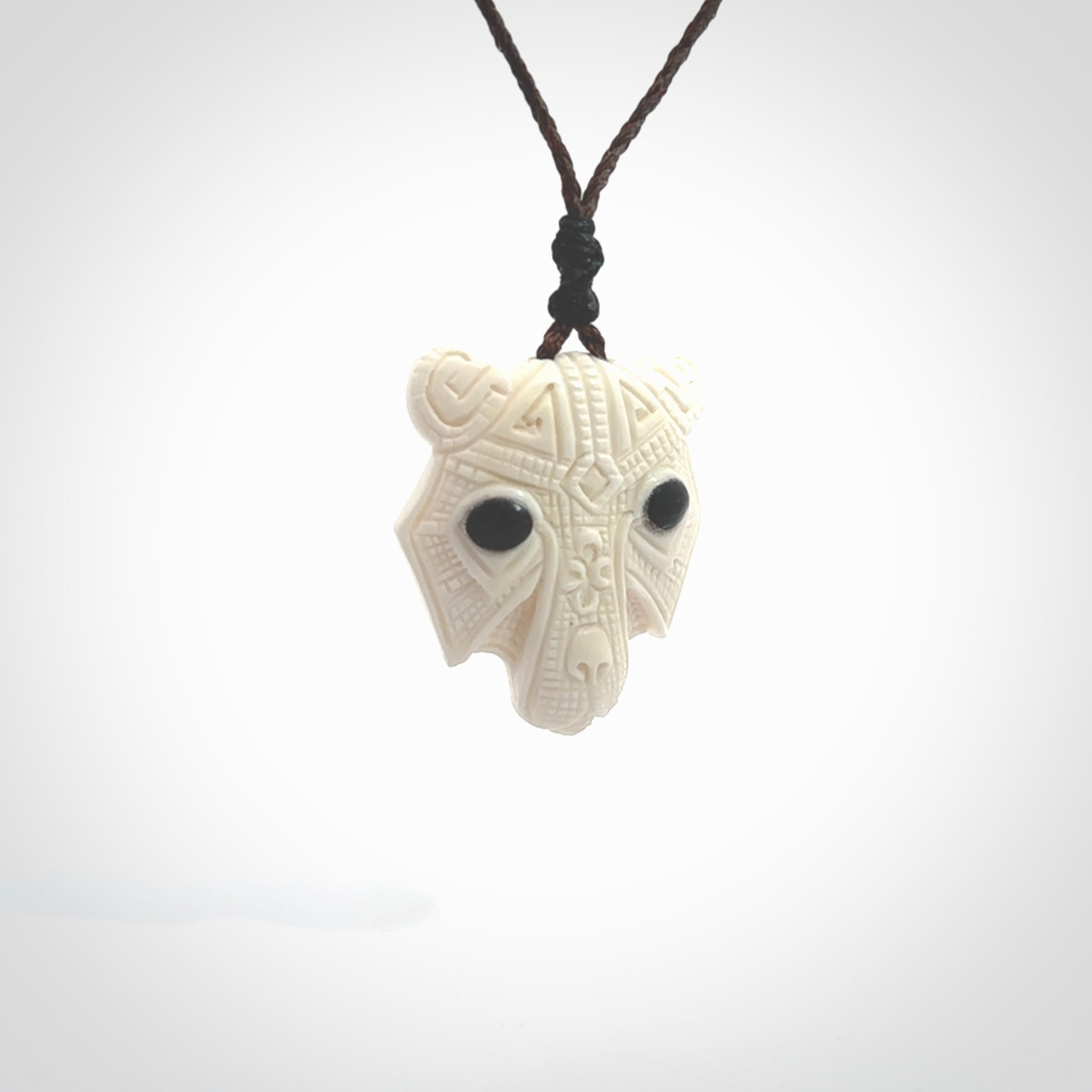 This picture shows a grizzly bear pendant that we designed in bone with buffalo horn inlay eyes. It is a grizzly bear head that is carved in detail. A really attractive and eye-catching piece of handmade jewellery. The cord is hand plaited braid in brown and the length can be adjusted.