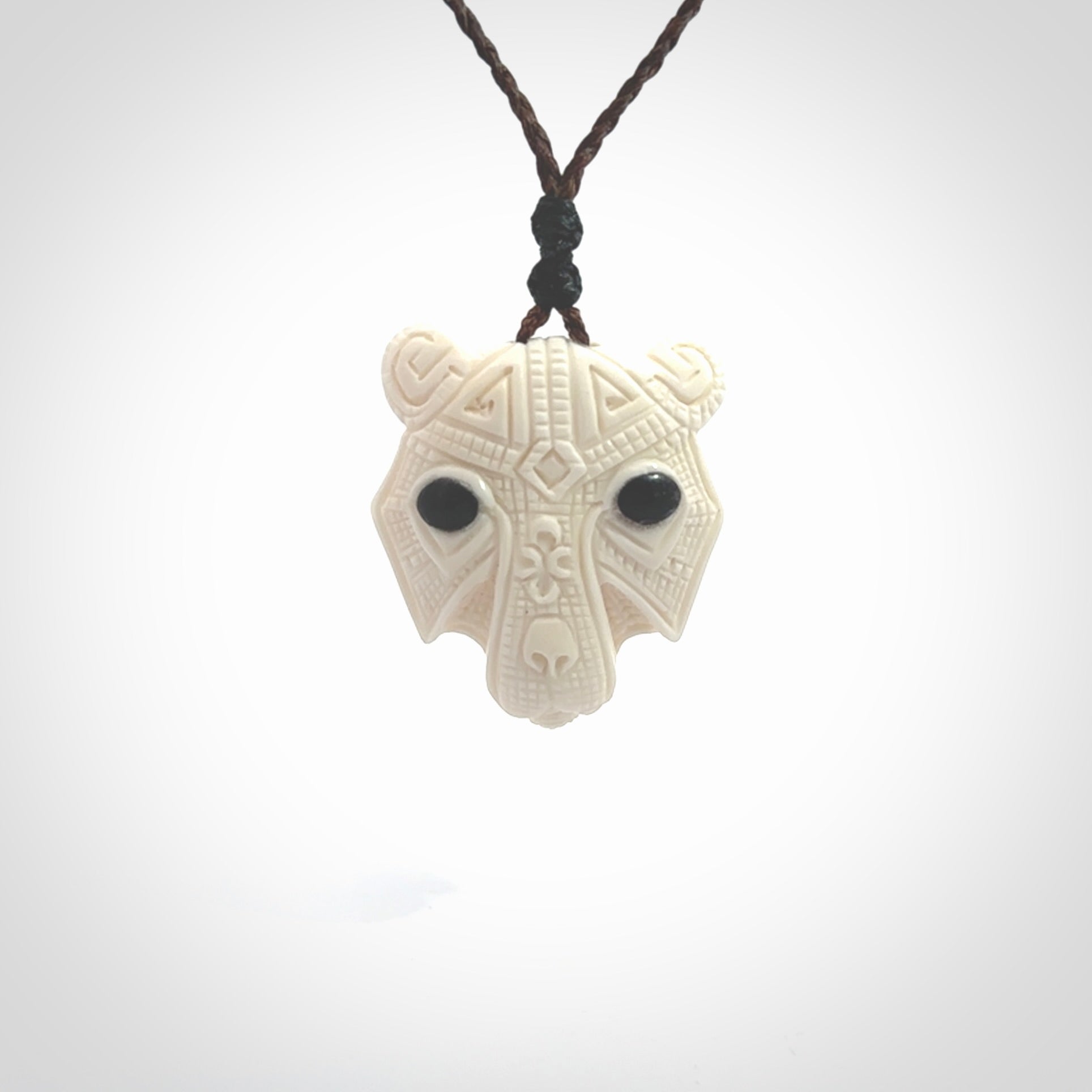 This picture shows a grizzly bear pendant that we designed in bone with buffalo horn inlay eyes. It is a grizzly bear head that is carved in detail. A really attractive and eye-catching piece of handmade jewellery. The cord is hand plaited braid in brown and the length can be adjusted.