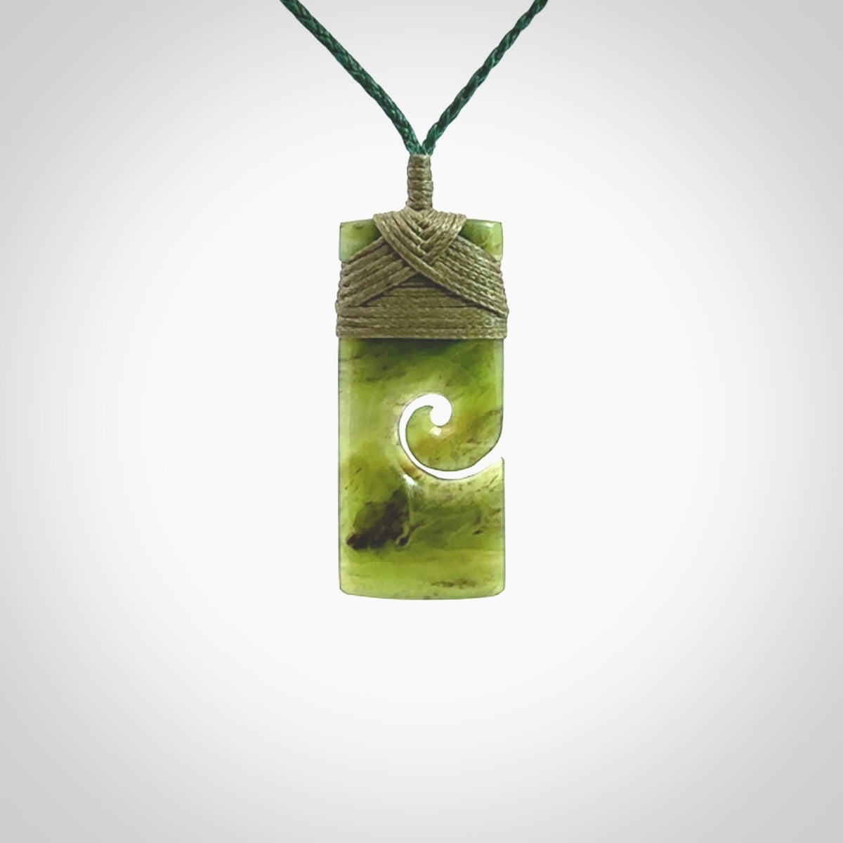 This picture shows a small toki pendant with a koru carved into the side. The cord is plaited and is length adjustable. This is a small toki pendant carved from beautiful New Zealand jade.