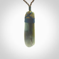 This photo shows a beautiful Inanga jade toki suspended from a hand plaited adjustable cord. The binding around the top of the toki is a blue and khaki green colour. The cord is length adjustable which allows the pendant to be positioned where it suits you best. The toki was carved for us by Jen Hung who is a master jade carver from New Zealand.