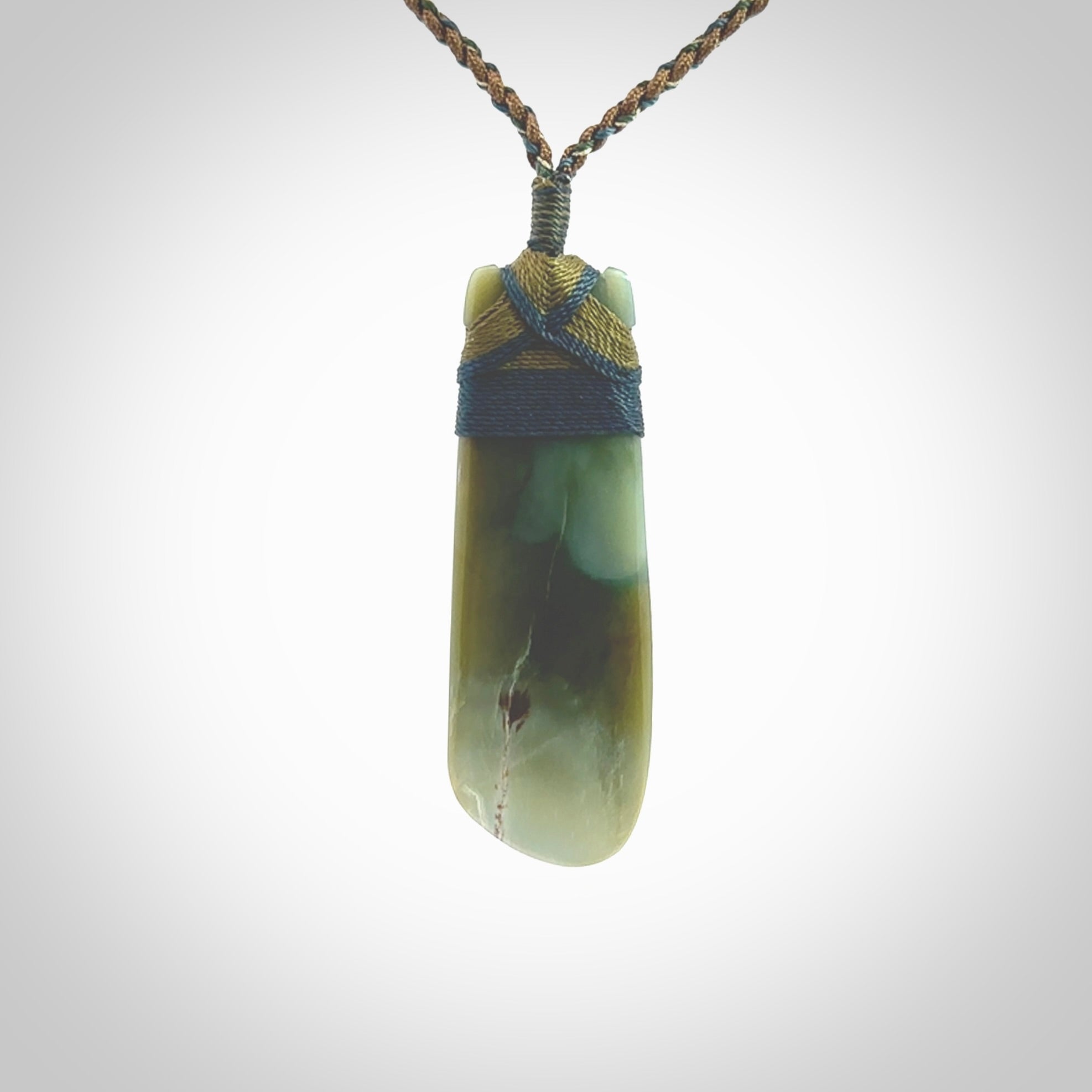 This photo shows a beautiful Inanga jade toki suspended from a hand plaited adjustable cord. The binding around the top of the toki is a blue and khaki green colour. The cord is length adjustable which allows the pendant to be positioned where it suits you best. The toki was carved for us by Jen Hung who is a master jade carver from New Zealand.