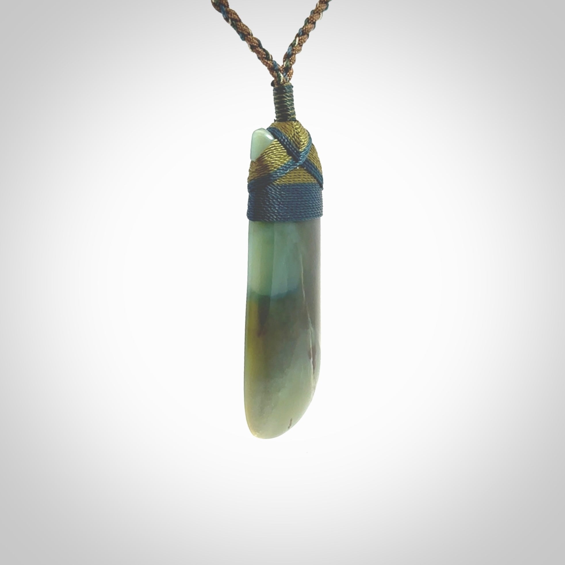 This photo shows a beautiful Inanga jade toki suspended from a hand plaited adjustable cord. The binding around the top of the toki is a blue and khaki green colour. The cord is length adjustable which allows the pendant to be positioned where it suits you best. The toki was carved for us by Jen Hung who is a master jade carver from New Zealand.