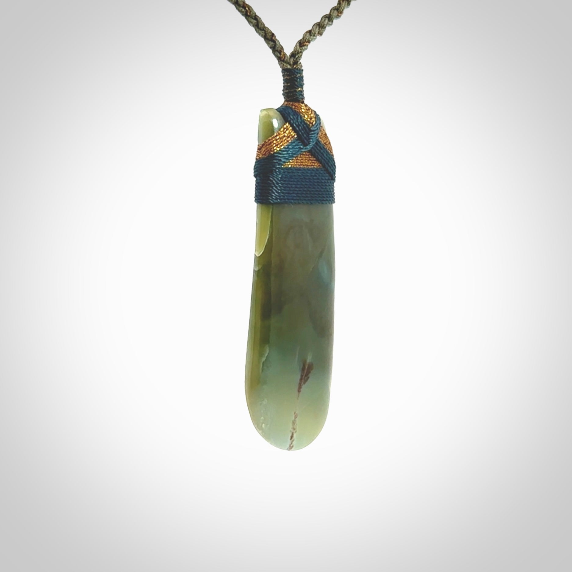 This photo shows a beautiful Inanga jade toki suspended from a hand plaited adjustable cord. The binding around the top of the toki is a blue and brown colour. The cord is length adjustable which allows the pendant to be positioned where it suits you best. The toki was carved for us by Jen Hung who is a wonderful jade carver from New Zealand.