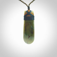 This photo shows a beautiful Inanga jade toki suspended from a hand plaited adjustable cord. The binding around the top of the toki is a blue and brown colour. The cord is length adjustable which allows the pendant to be positioned where it suits you best. The toki was carved for us by Jen Hung who is a wonderful jade carver from New Zealand.