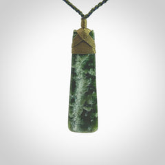 This photo shows a beautiful New Zealand jade toki suspended from a hand plaited adjustable cord. The binding around the top of the toki is a khaki green colour. The cord is length adjustable which allows the pendant to be positioned where it suits you best. The toki was carved for us by Jen Hung who is a wonderful jade carver from New Zealand.