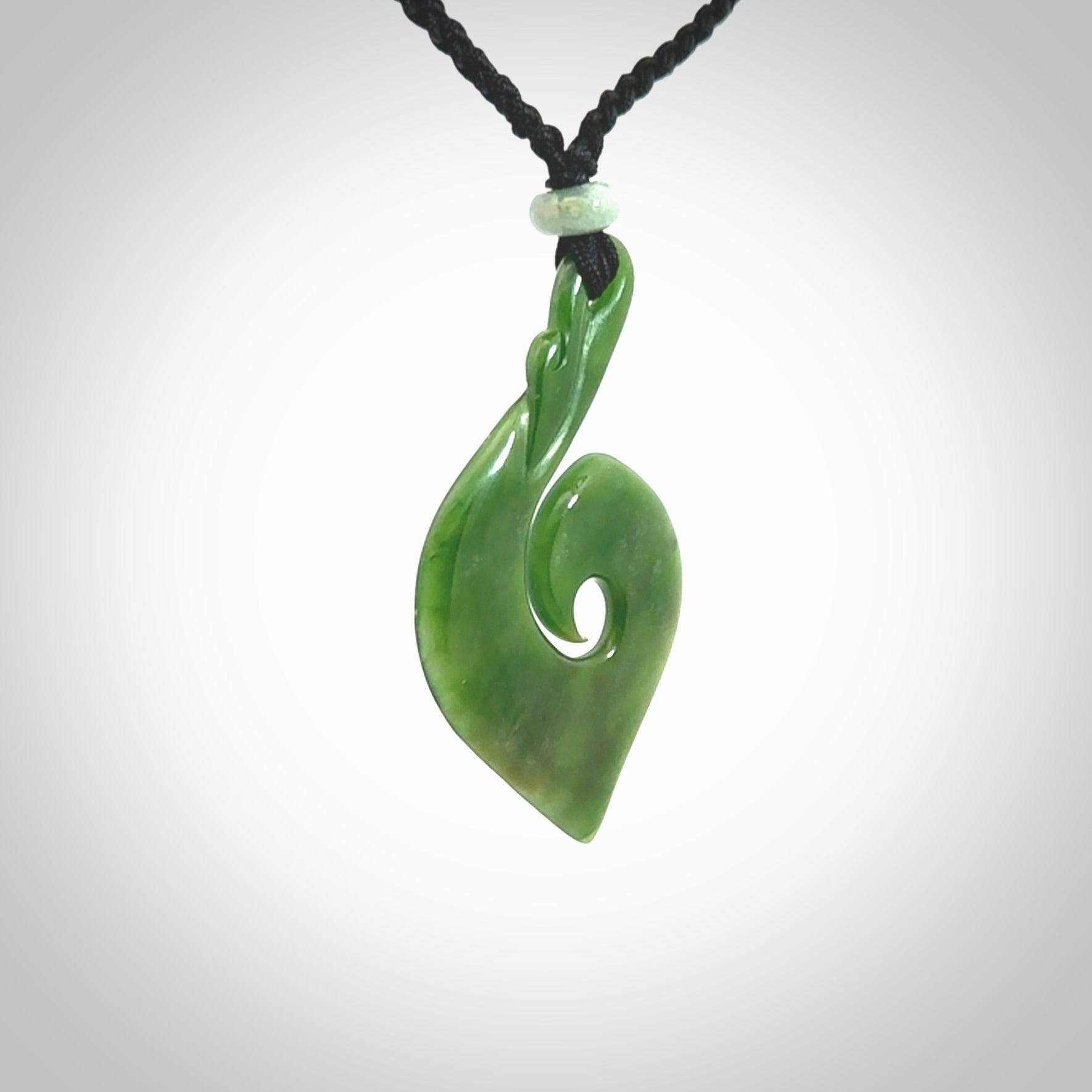 This photo shows a beautiful jade swan hook suspended from a hand plaited black cord. This swan hook was carved for us by Jen Hung who is a master jade carver from New Zealand.