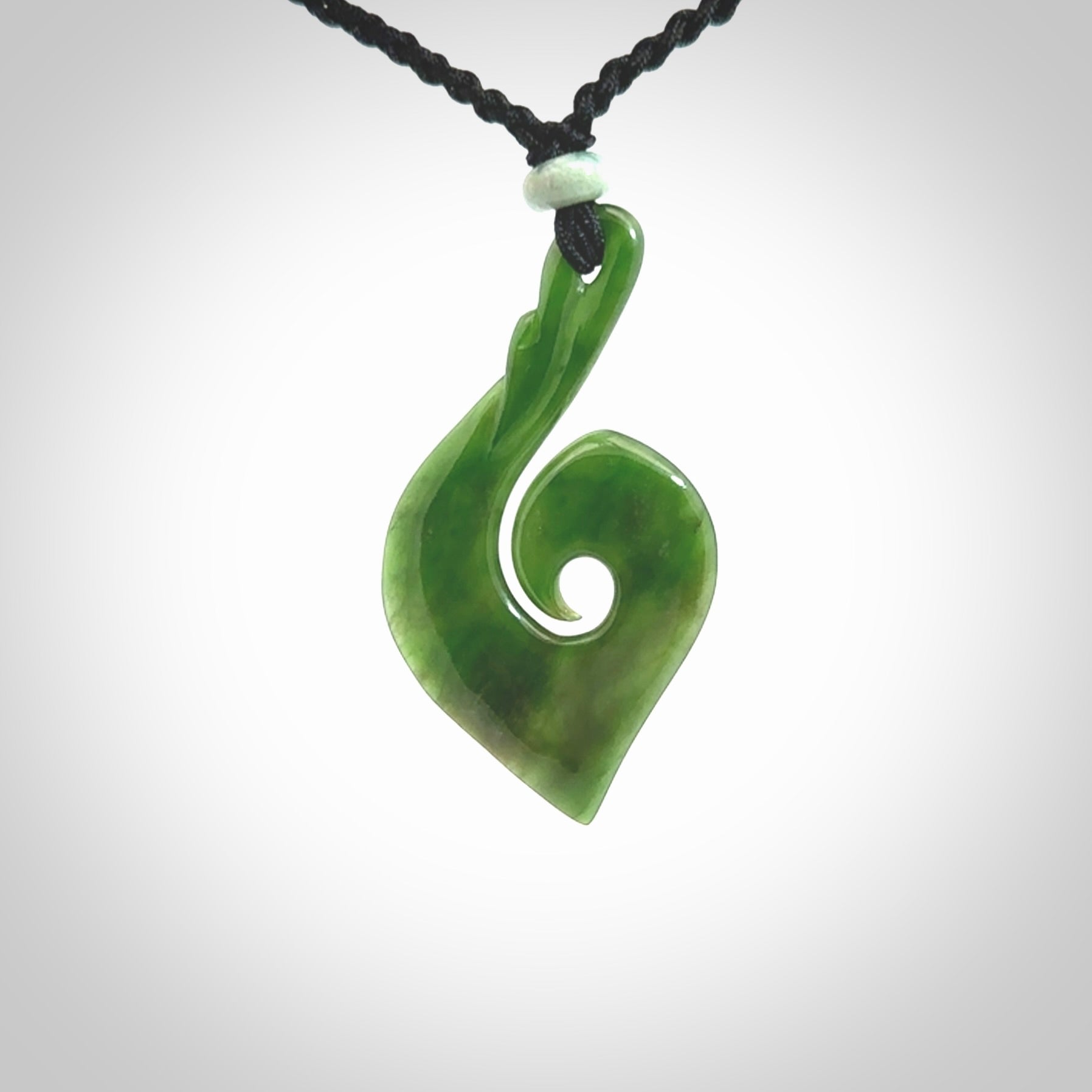 This photo shows a beautiful jade swan hook suspended from a hand plaited black cord. This swan hook was carved for us by Jen Hung who is a master jade carver from New Zealand.