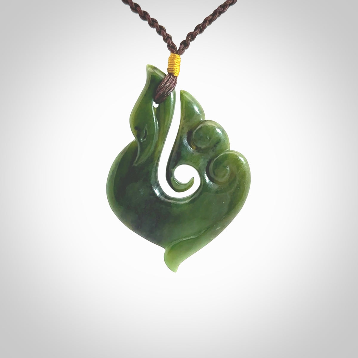 This photo shows a beautiful jade swan hook suspended from a hand plaited brown cord. This swan hook was carved for us by Jen Hung who is a master jade carver from New Zealand.