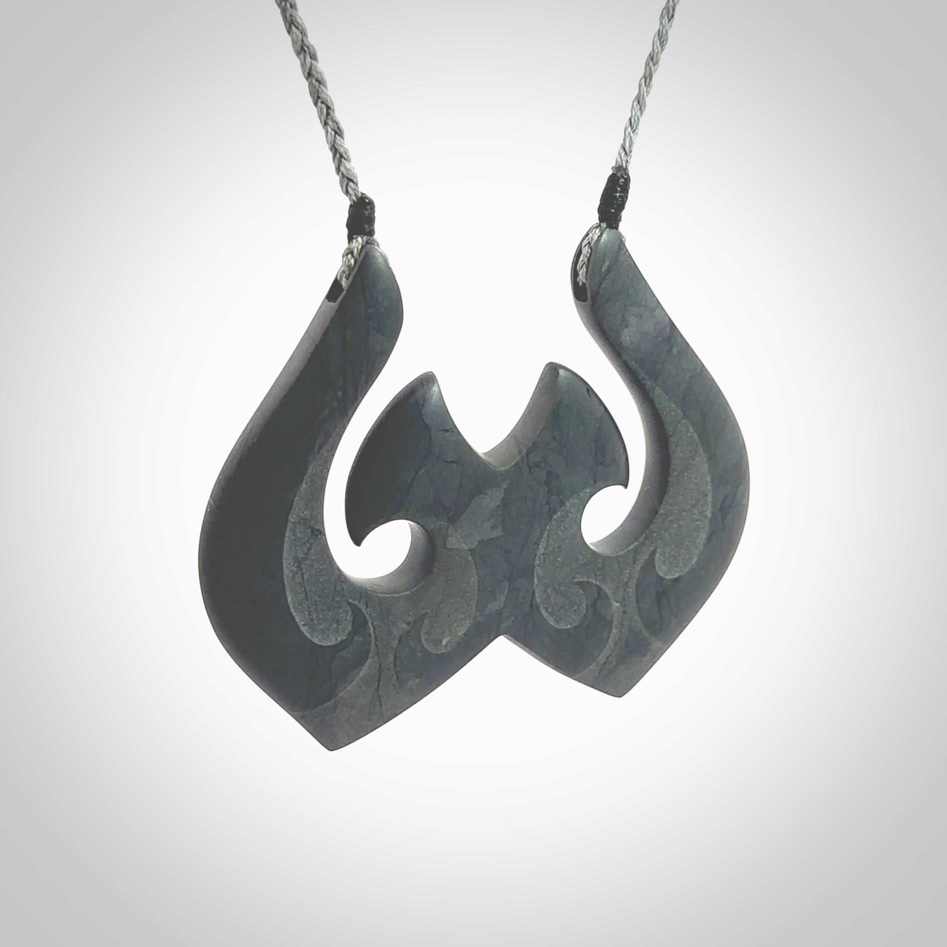 A hand carved large New Zealand Argillite double Hook, Matau, necklace. The cord is a grey colour and is adjustable in length. A large sized hand made double hook necklace by New Zealand artist Rueben Tipene. One off work of art to wear.