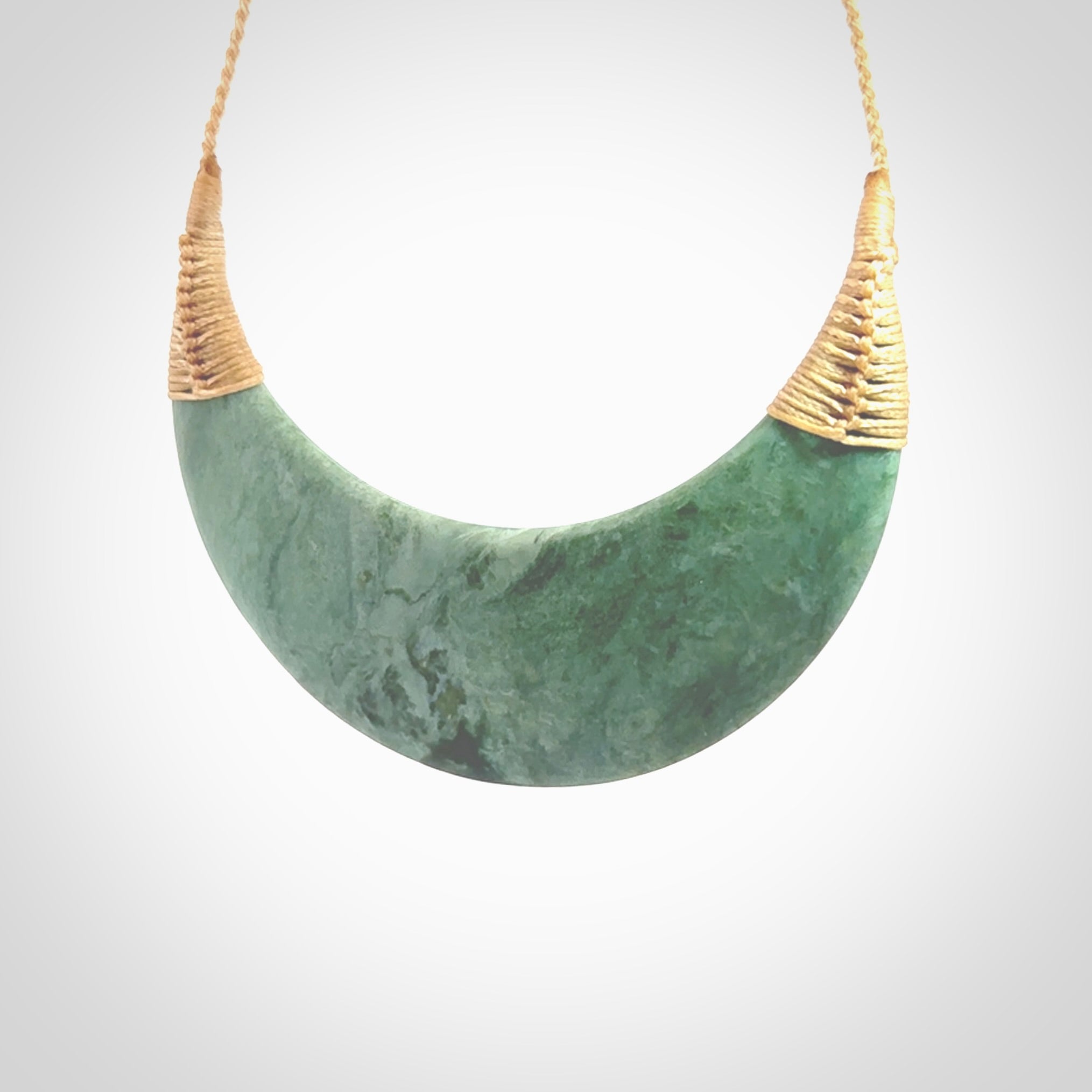 This picture shows a hand carved New Zealand Inanga jade contemporary half-shield pendant. It is a light blue and green colour and is a wonderful, large piece of jewellery. The cord is hand plaited and adjustable so that you can position the pendant where it suits you best. This piece was carved for us by Kyohei Noguchi. Delivery is free worldwide.