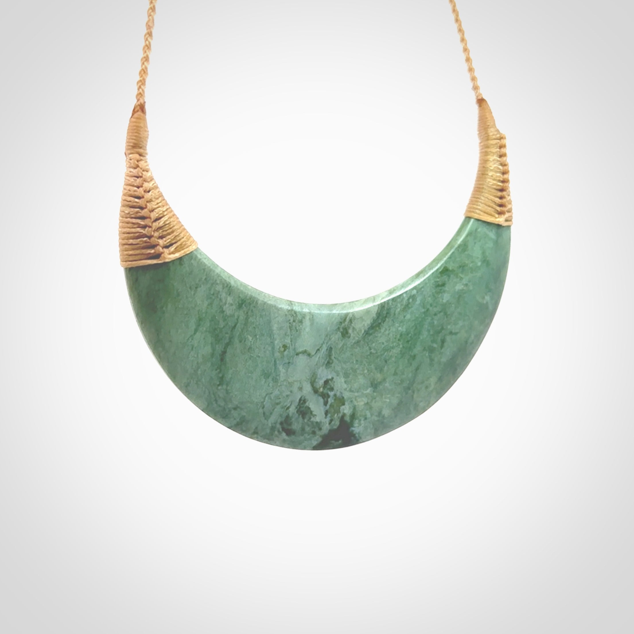 This picture shows a hand carved New Zealand Inanga jade contemporary half-shield pendant. It is a light blue and green colour and is a wonderful, large piece of jewellery. The cord is hand plaited and adjustable so that you can position the pendant where it suits you best. This piece was carved for us by Kyohei Noguchi. Delivery is free worldwide.