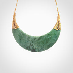 This picture shows a hand carved New Zealand Inanga jade contemporary half-shield pendant. It is a light blue and green colour and is a wonderful, large piece of jewellery. The cord is hand plaited and adjustable so that you can position the pendant where it suits you best. This piece was carved for us by Kyohei Noguchi. Delivery is free worldwide.