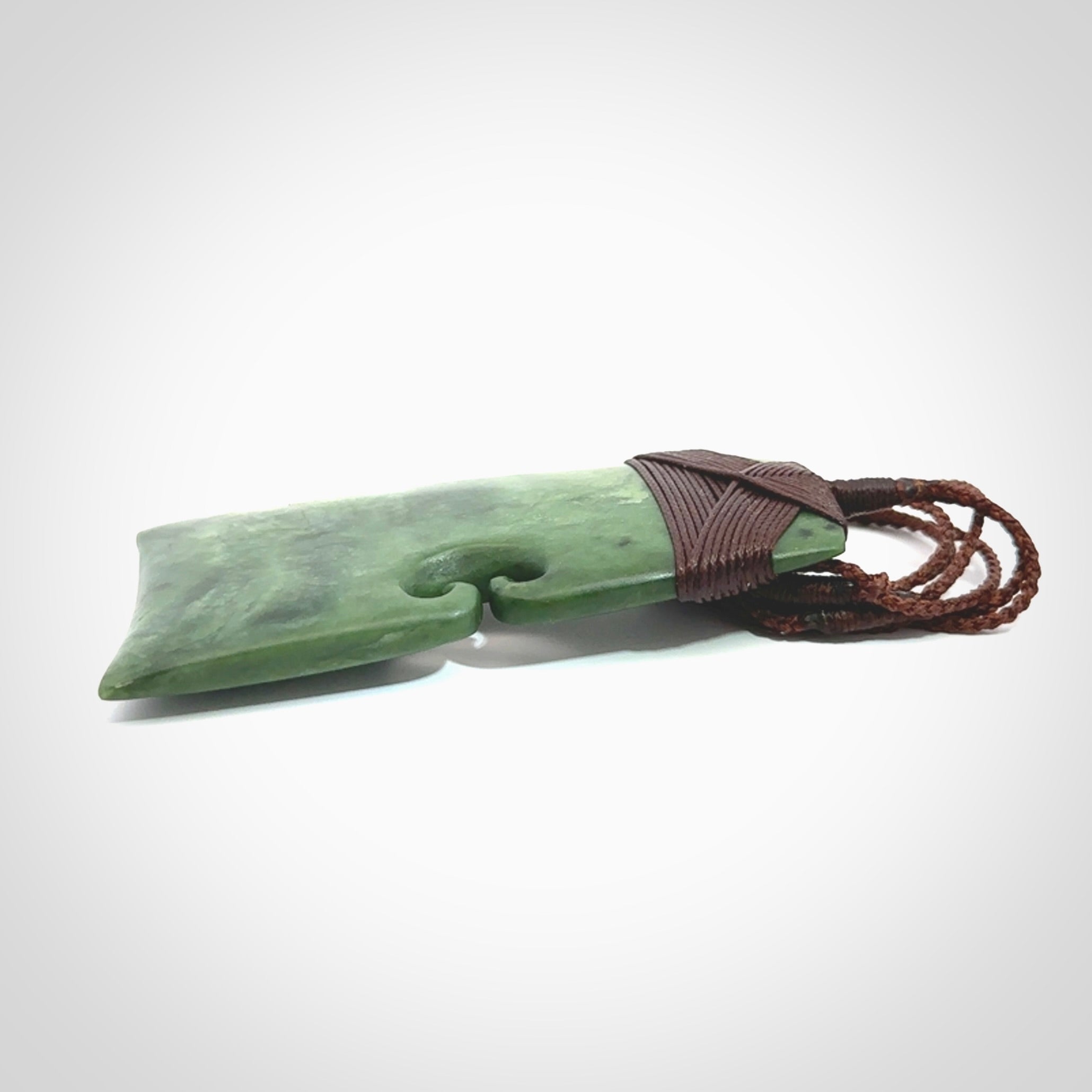 This is a lovely, one-off large green toki pendant hand made from a gorgeous New Zealand jade. It is finished in a matte sheen and is bound with a dark brown plaited cord. This toki has a koru carved into the side of the blade. This is a wonderful piece that is very attractive and will last a lifetime. Hand carved by Kyohei Noguchi.