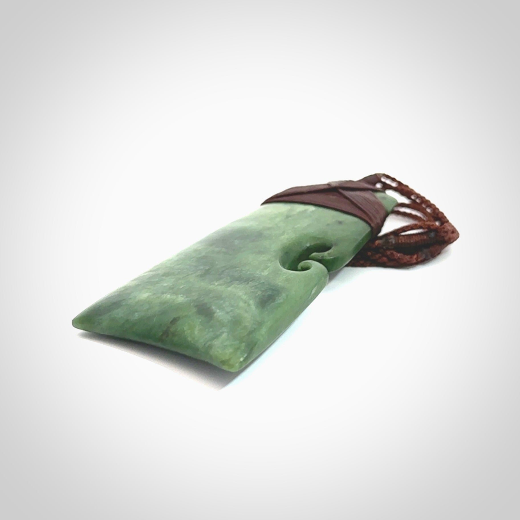 This is a lovely, one-off large green toki pendant hand made from a gorgeous New Zealand jade. It is finished in a matte sheen and is bound with a dark brown plaited cord. This toki has a koru carved into the side of the blade. This is a wonderful piece that is very attractive and will last a lifetime. Hand carved by Kyohei Noguchi.