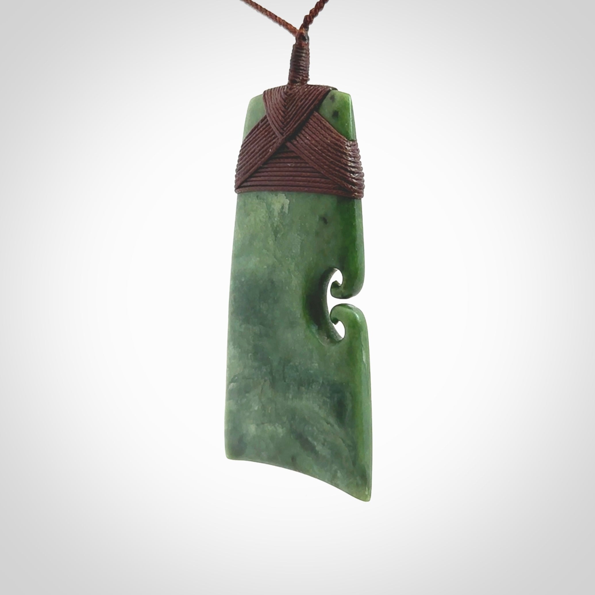 This is a lovely, one-off large green toki pendant hand made from a gorgeous New Zealand jade. It is finished in a matte sheen and is bound with a dark brown plaited cord. This toki has a koru carved into the side of the blade. This is a wonderful piece that is very attractive and will last a lifetime. Hand carved by Kyohei Noguchi.