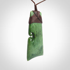 This is a lovely, one-off large green toki pendant hand made from a gorgeous New Zealand jade. It is finished in a matte sheen and is bound with a dark brown plaited cord. This toki has a koru carved into the side of the blade. This is a wonderful piece that is very attractive and will last a lifetime. Hand carved by Kyohei Noguchi.