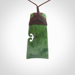 This is a lovely, one-off large green toki pendant hand made from a gorgeous New Zealand jade. It is finished in a matte sheen and is bound with a dark brown plaited cord. This toki has a koru carved into the side of the blade. This is a wonderful piece that is very attractive and will last a lifetime. Hand carved by Kyohei Noguchi.